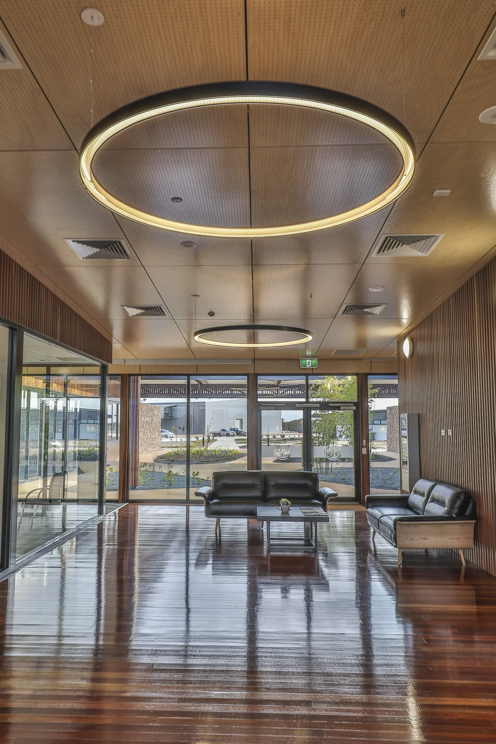 Contemporary commercial lobby featuring floor-to-ceiling glazing, timber wall panelling, polished timber flooring and views to a landscaped courtyard.
