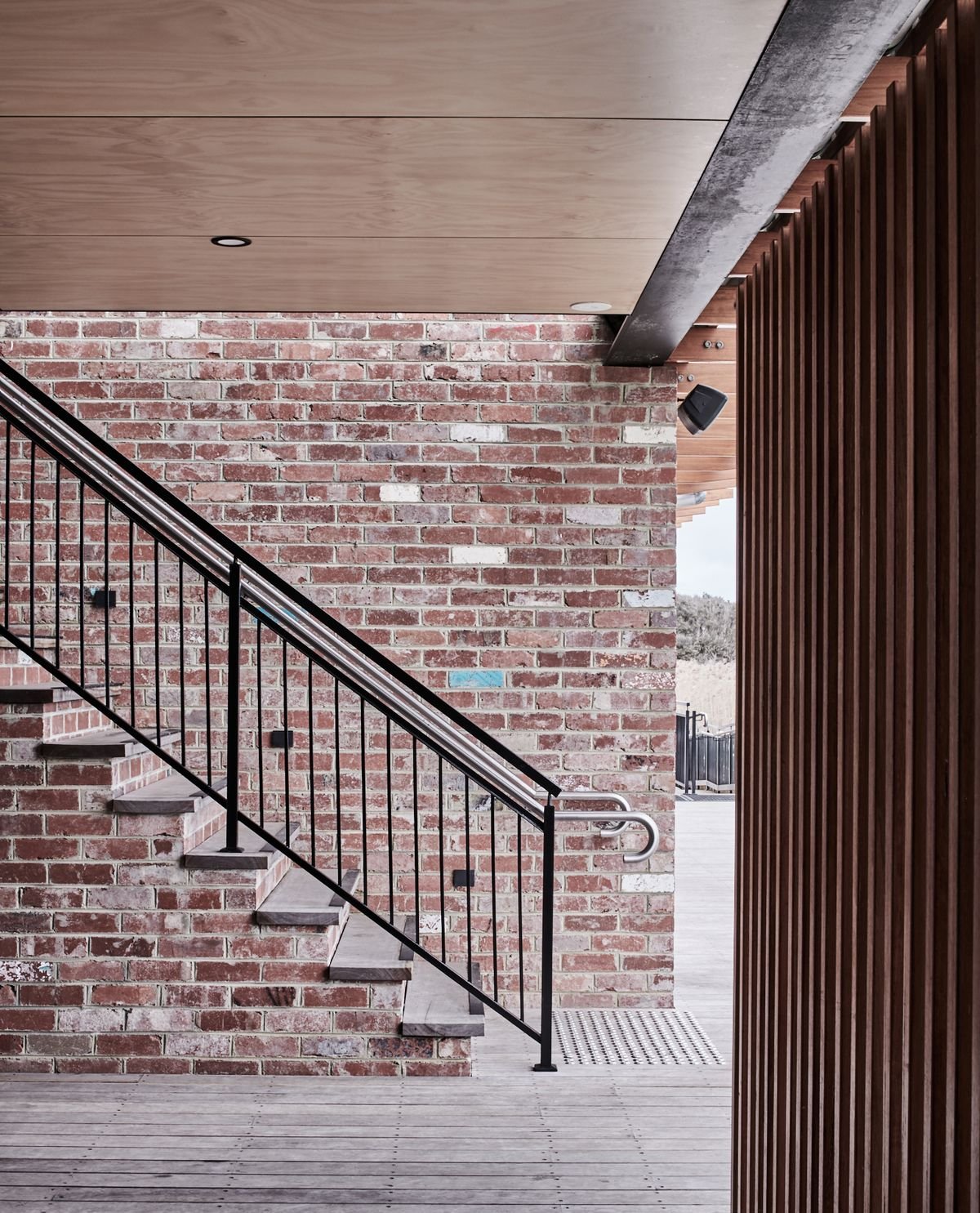 Exterior detail of a brick building with a steel staircase, timber screening and contemporary architectural finishes.