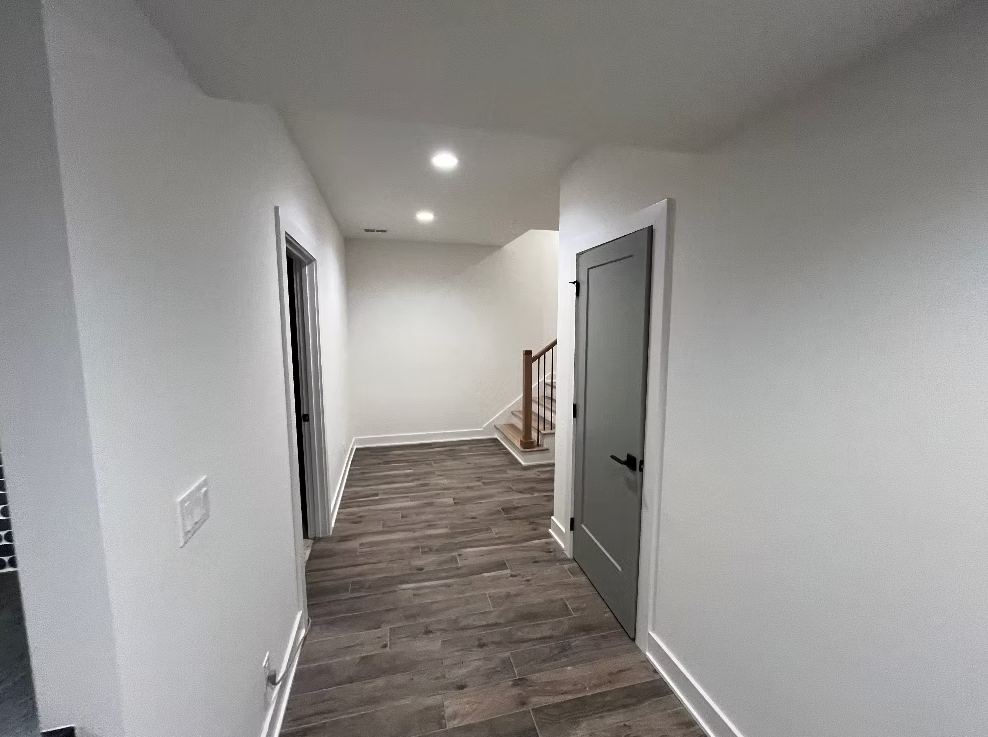 Empty hallway in a house with white walls, dark wood floors, and a gray door.