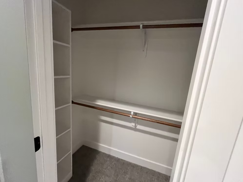 Empty walk-in closet with white walls, shelves on the side, and wooden closet rods.