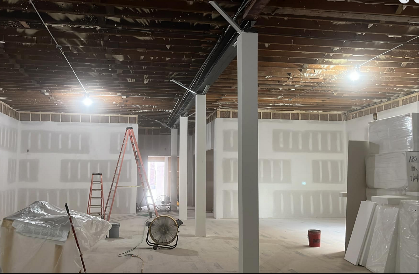 Interior of a construction site with drywall installation, ladders, and construction tools in a partially finished room.