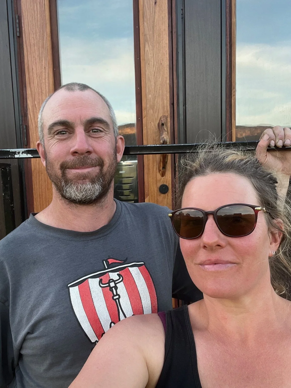 A man and a woman taking a selfie outside the sauna they have built, during sunset or late afternoon in the Megalong Valley.