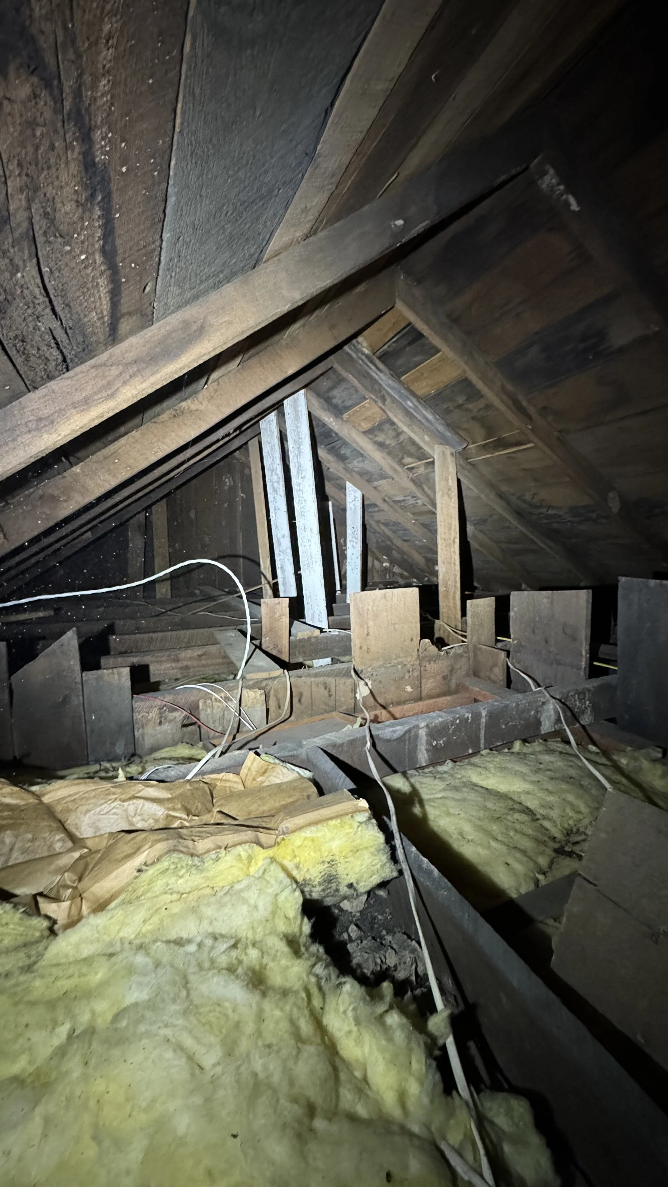 Attic space with exposed wooden beams, insulation, and electrical wiring.