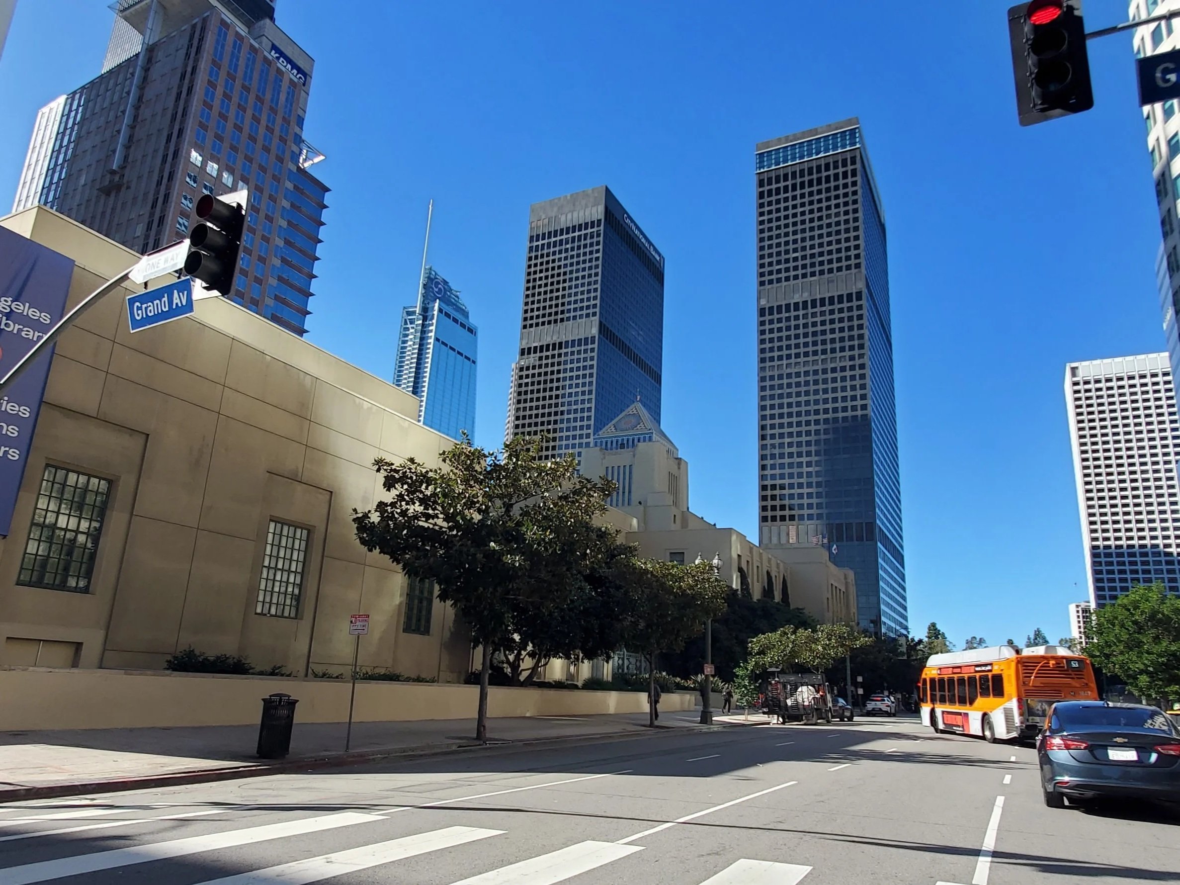 A street scene in San Francisco, with tall buildings, a blue sky, a traffic light, street signs, trees, a bus, and cars.