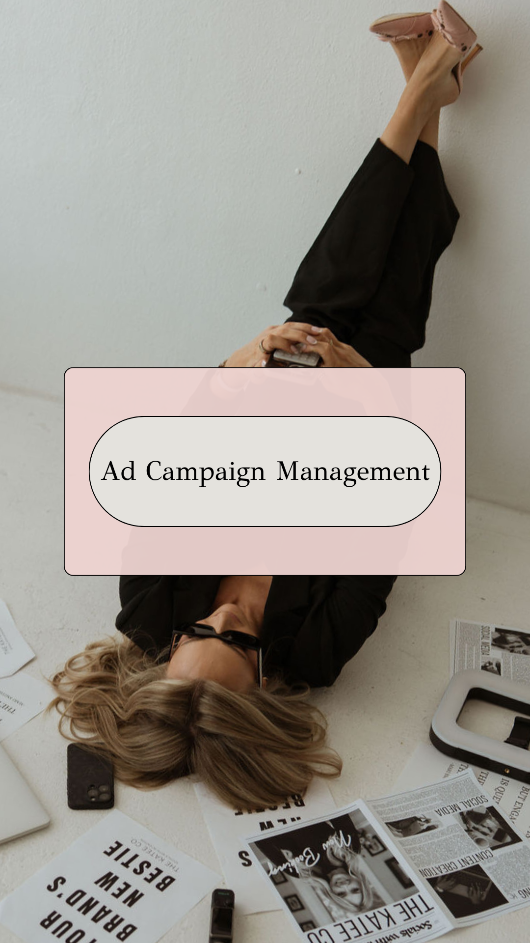 A woman lying on the floor surrounded by newspapers, magazines, a cell phone, and a white framed mirror, with a pink overlay with the text 'Ad Campaign Management'.