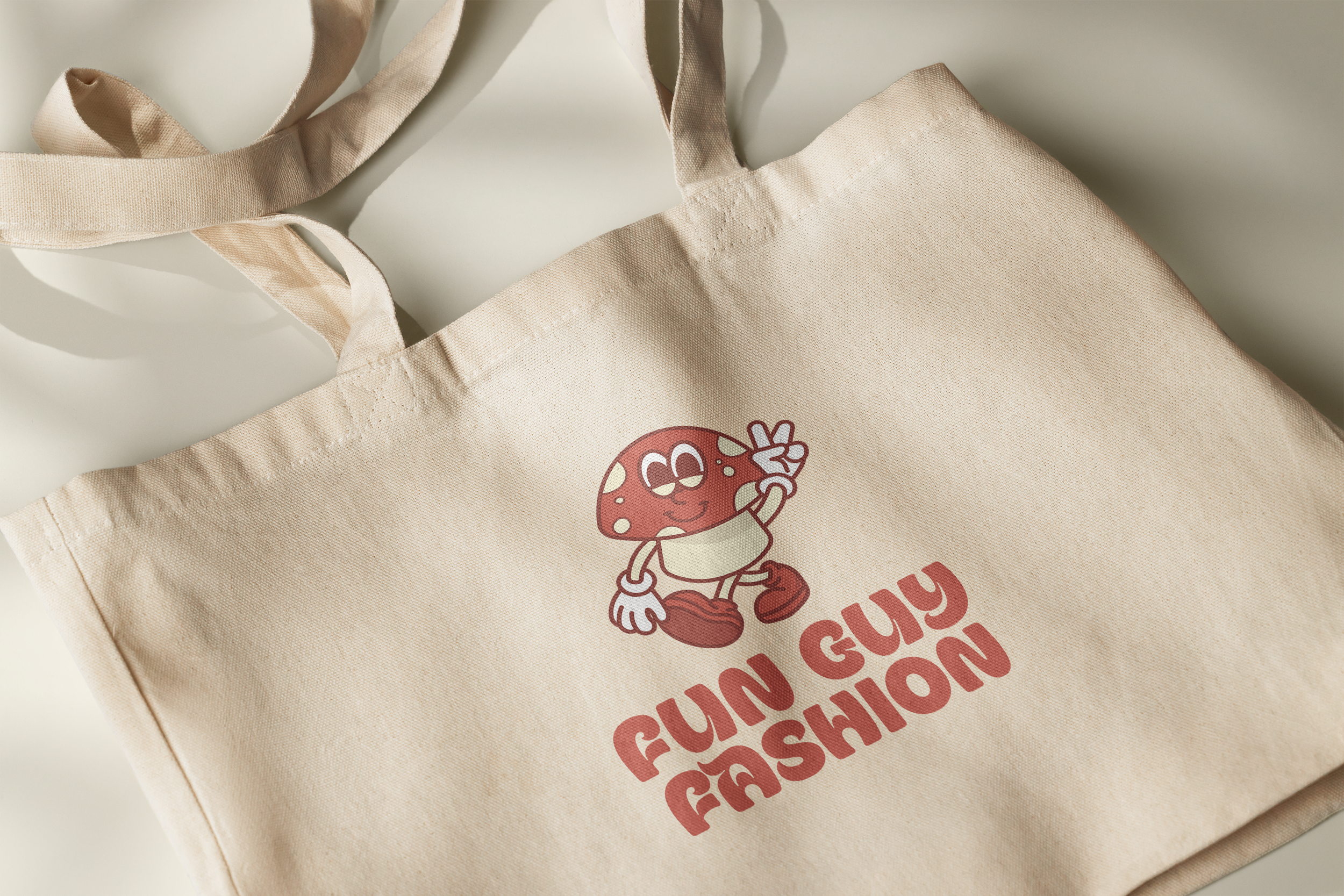 A beige tote bag with a cartoon mushroom character giving a peace sign and smiling, with the words "FUN GUY FASHION" printed below in pink text.