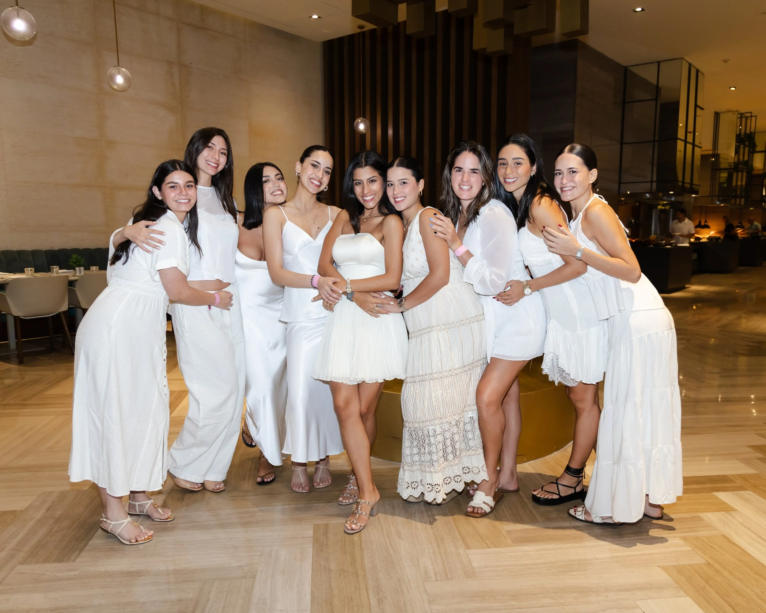 A group of ten women dressed in white standing together in a modern indoor setting, smiling at the camera.