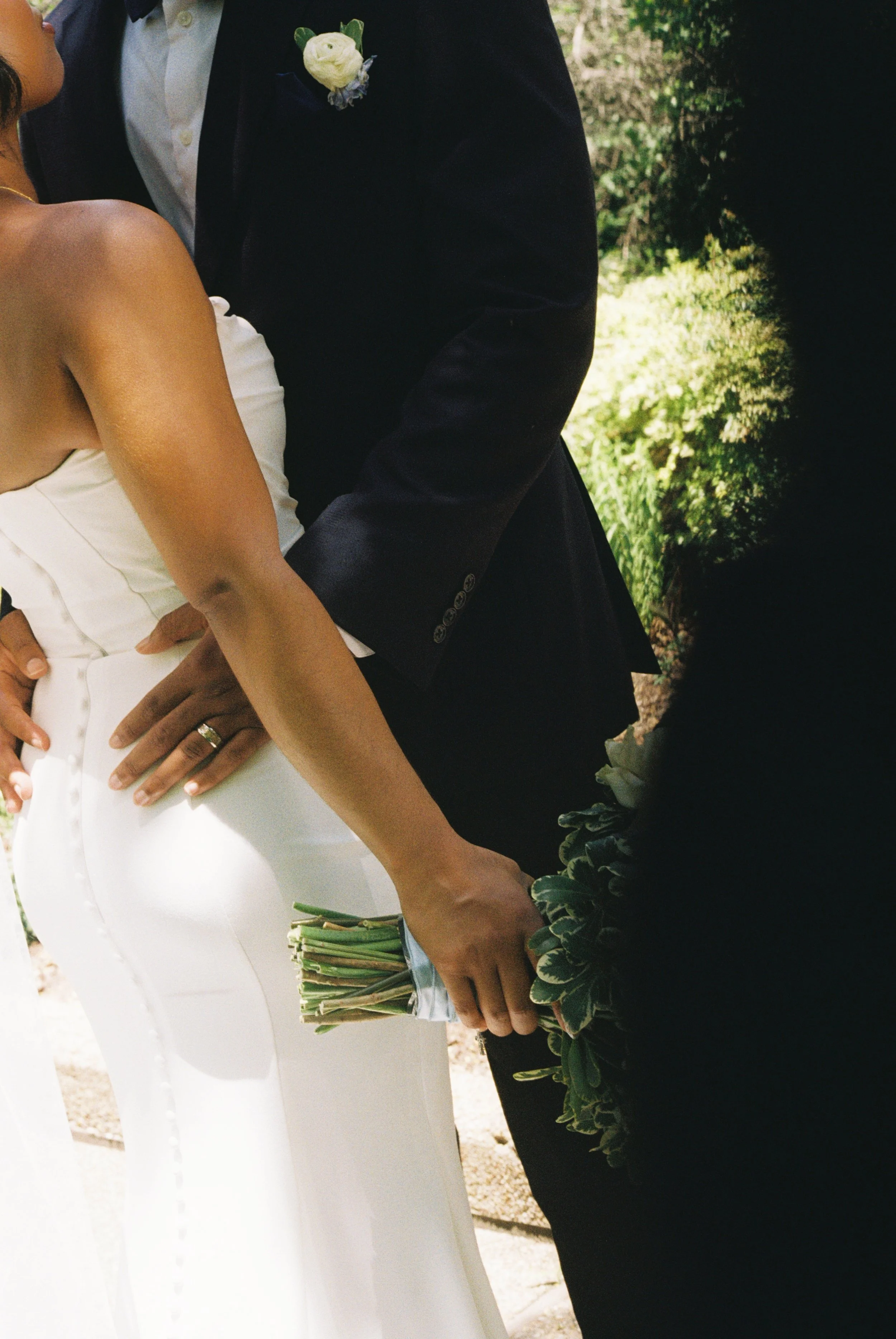 Close-up of a bride and groom during a wedding ceremony outdoors, with the bride holding a small bouquet of flowers.