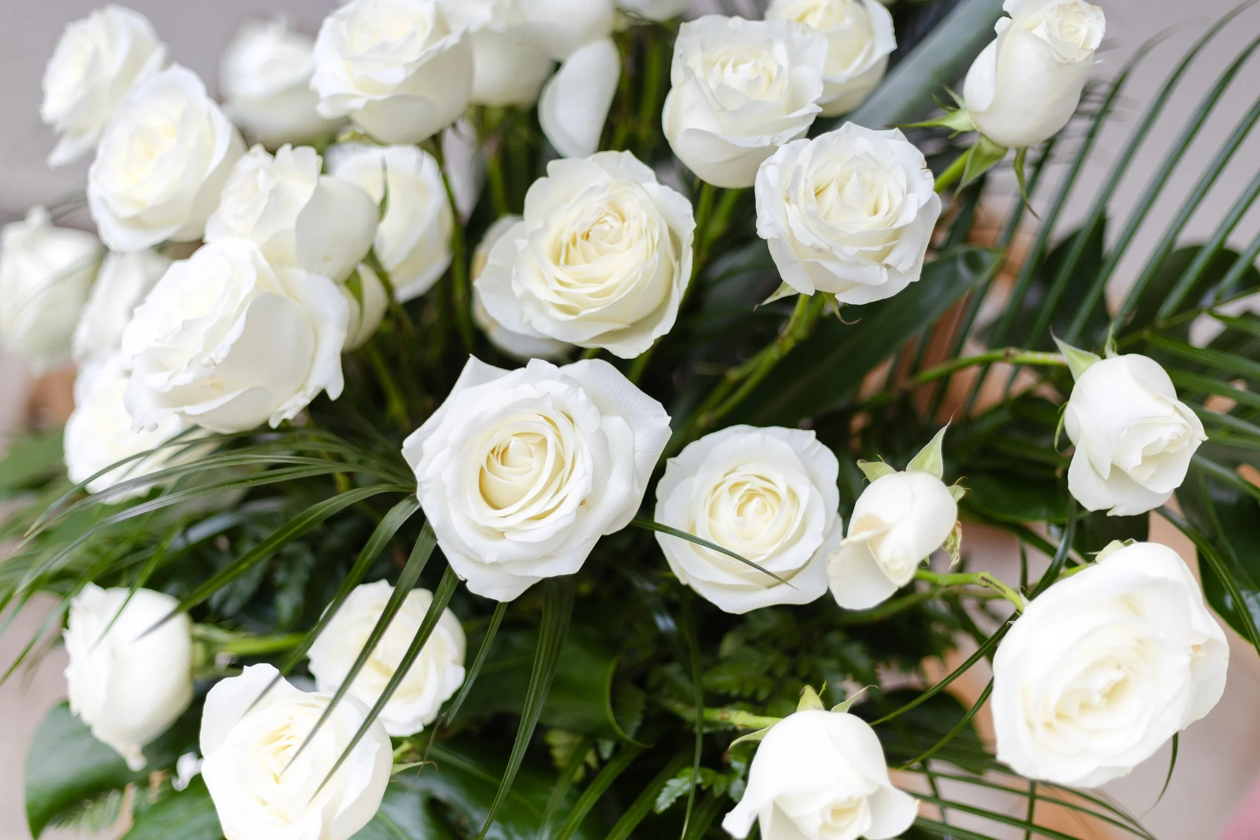 A bouquet of white roses with green leaves and long blades of grass.