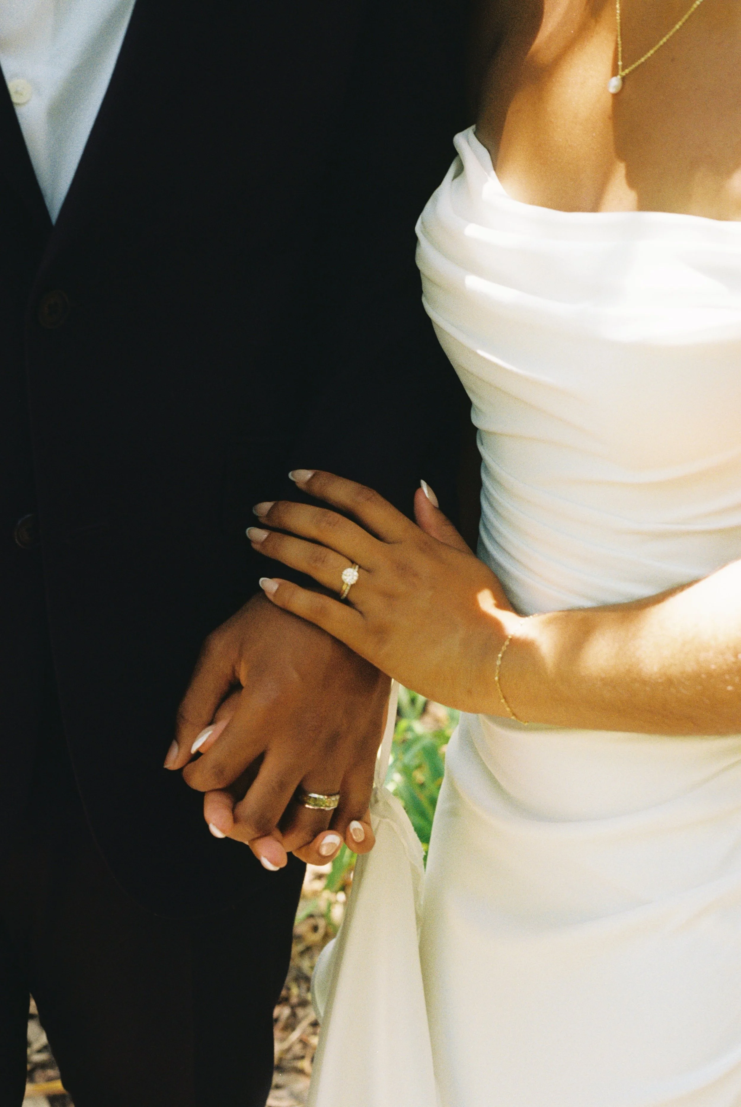 Close-up of a bride and groom holding hands during a wedding ceremony, focusing on their wedding rings and the bride's wedding dress and jewelry.