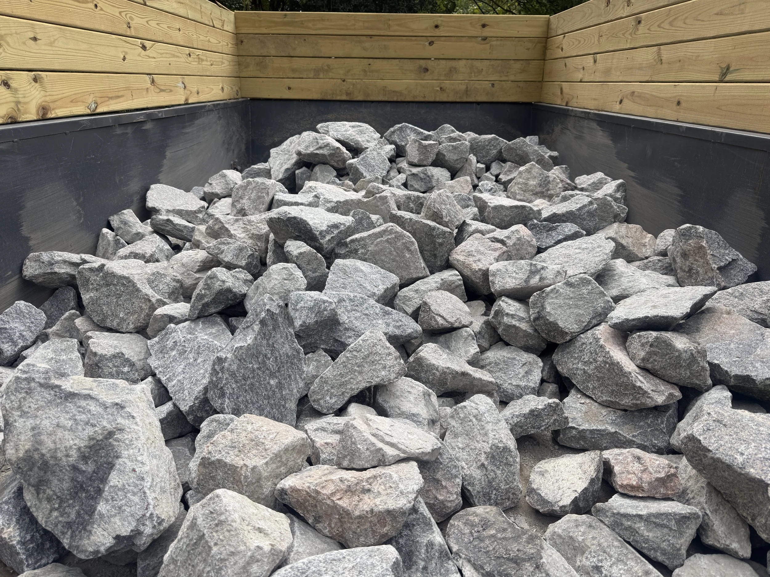 A corner of a wooden structure with a black waterproof barrier, filled with gray rocks or gravel.