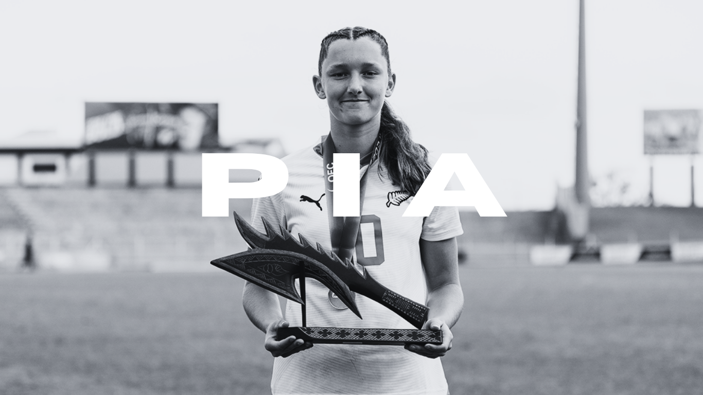 Young woman athlete holding a trophy shaped like a bird, standing on a sports field, with the word 'PIA' overlayed.