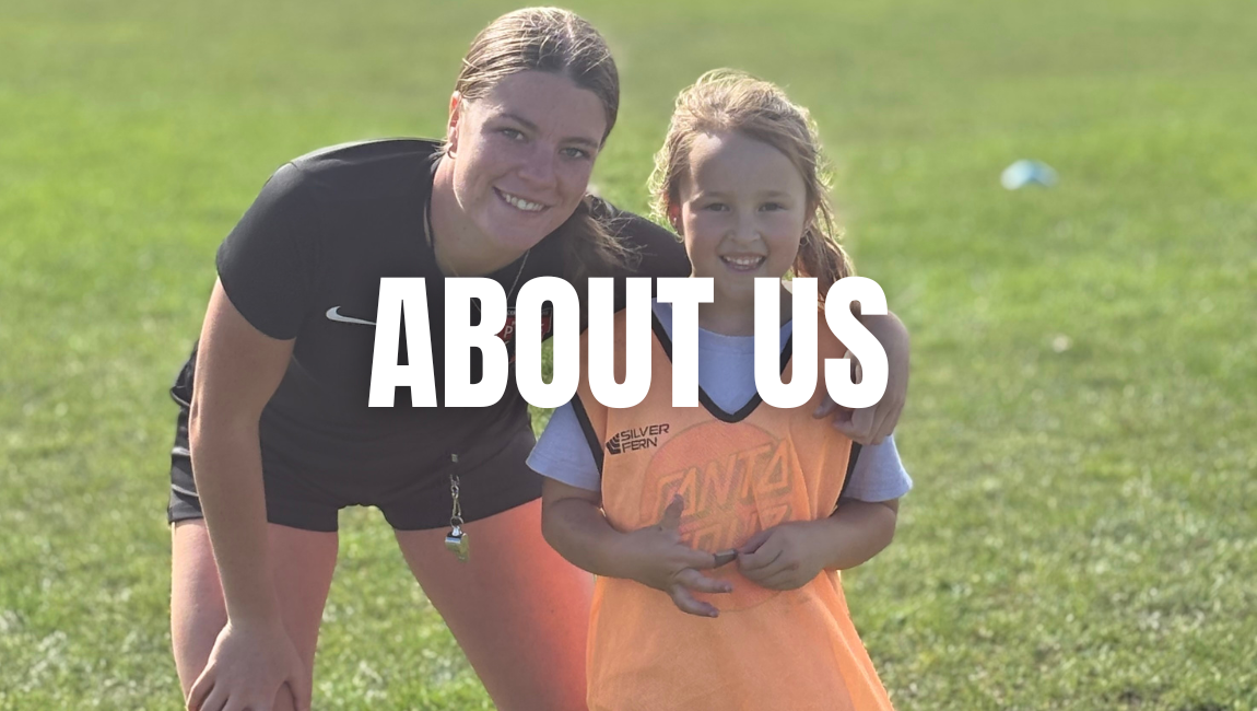 A woman and a young girl smiling on a grassy field, with the woman wearing a black sports shirt and the girl wearing an orange sports vest.