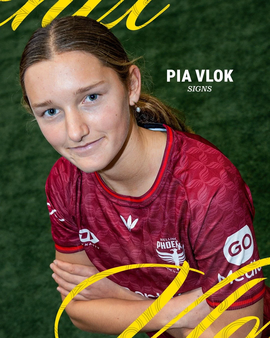 Close-up of Pia Vlok in a maroon sports jersey with team logo, looking at the camera with crossed arms, standing on green artificial turf.