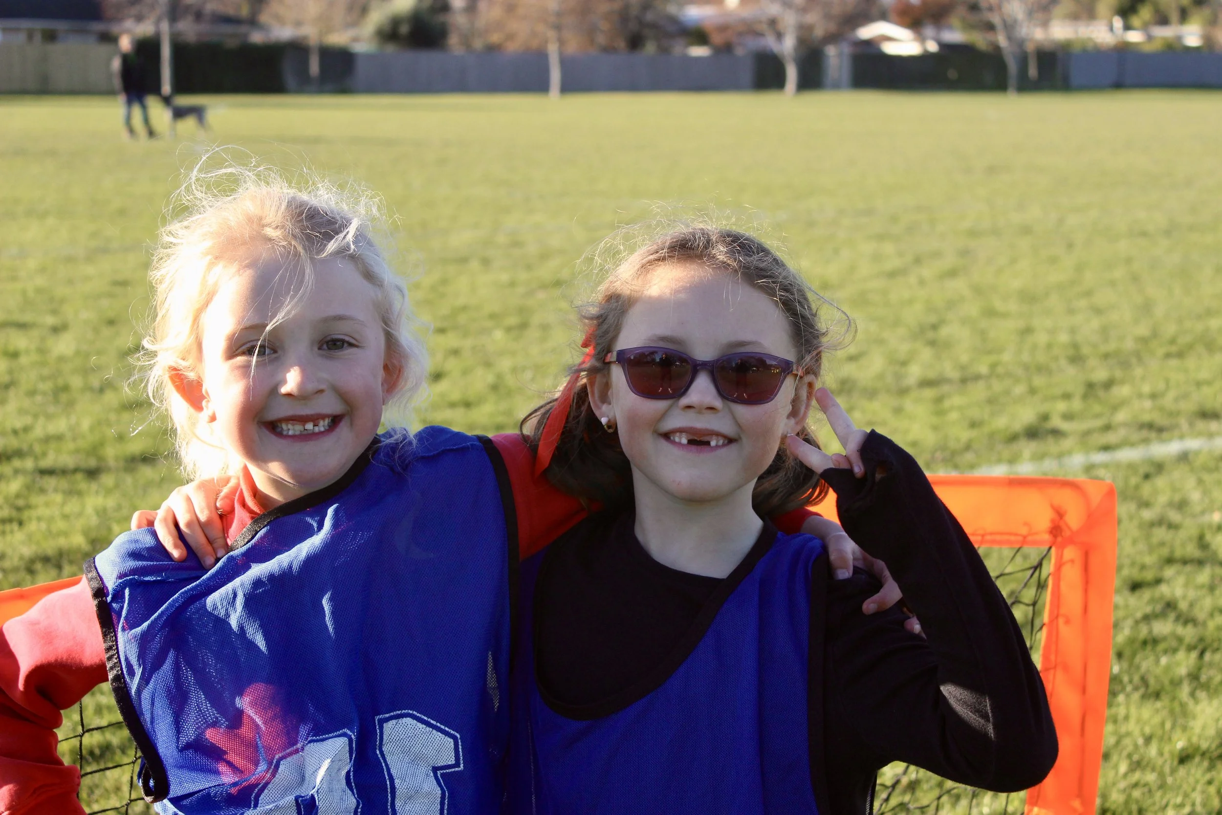 Children and an adult on a grassy field, with a playground in the background and a cloudy sky overhead.