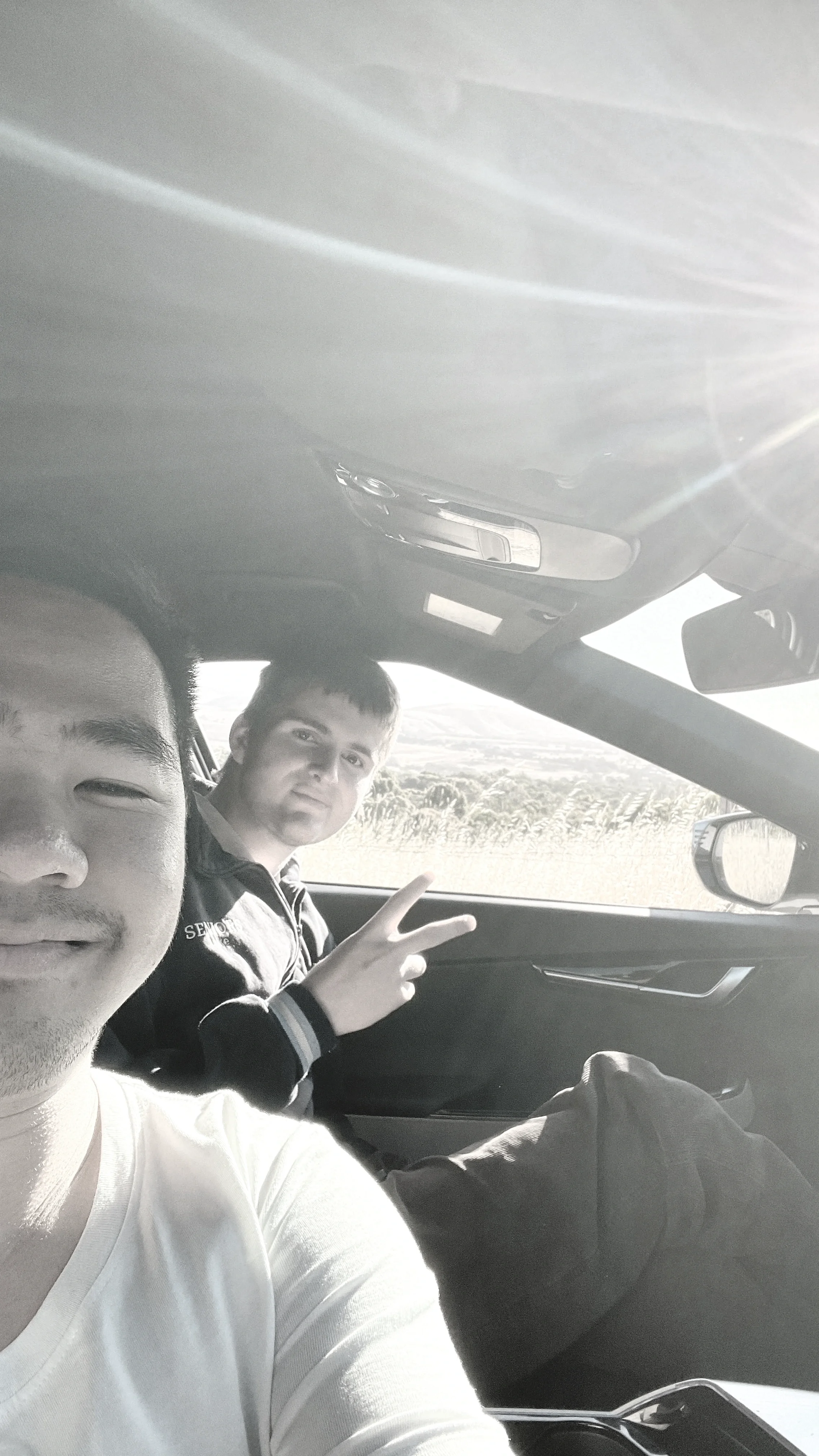Joel Chan and Luke Howis taking a selfie on a trip where they ended up taking stock of the songs God had given them. Outside the car window, there is a wide open space visible.