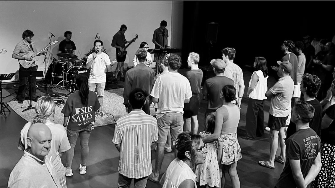 A group of people attending a live music session with a band playing, some people are standing and watching, while others are engaged in worship or prayer. This was vssls' first live worship night on January 26, 2026, the hottest day in SA, Aus
