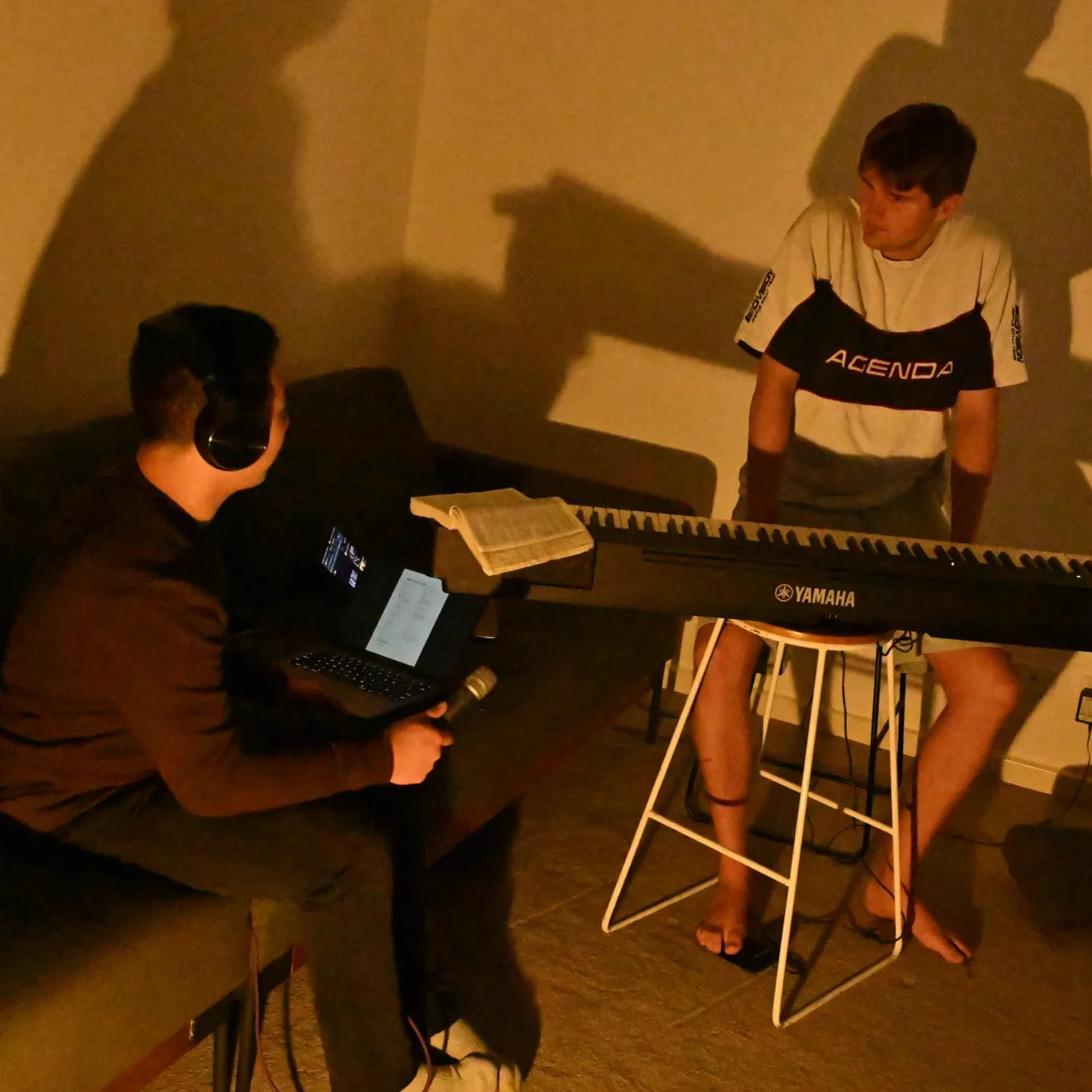 Joel and Luke, co-founders of vssls in a writing session. There is a bible on a Yamaha keyboard. One of the young men has a headphone and is holding a mic. Also in the picture is a laptop near the young men.