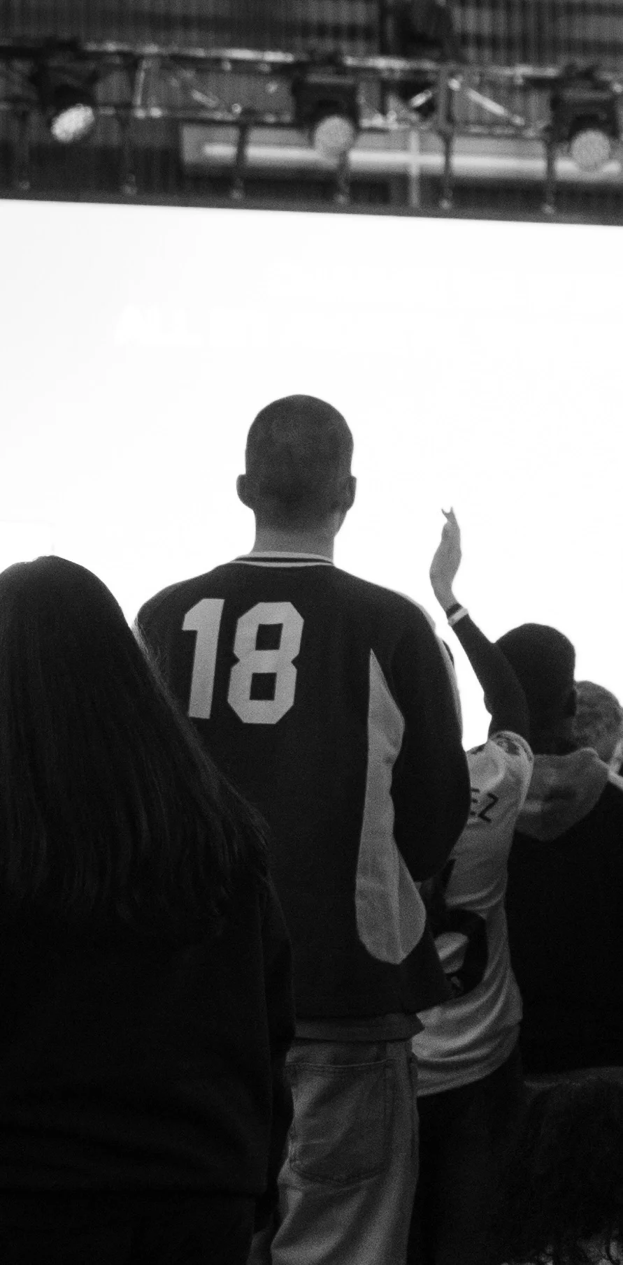 Luke, co-founder of vssls, in a sports jersey with the number 18 on the back, standing in front of a large bright screen, with other people nearby, some raising their hands in worship.