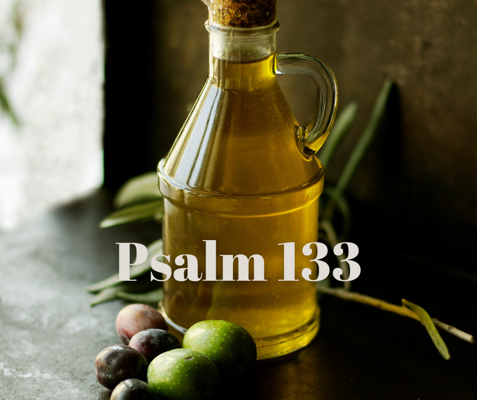 A glass bottle of olive oil with a cork on top, placed on a dark surface with green and purple olives and green leaves nearby, against a dark background, text 'Psalm' overlaid.