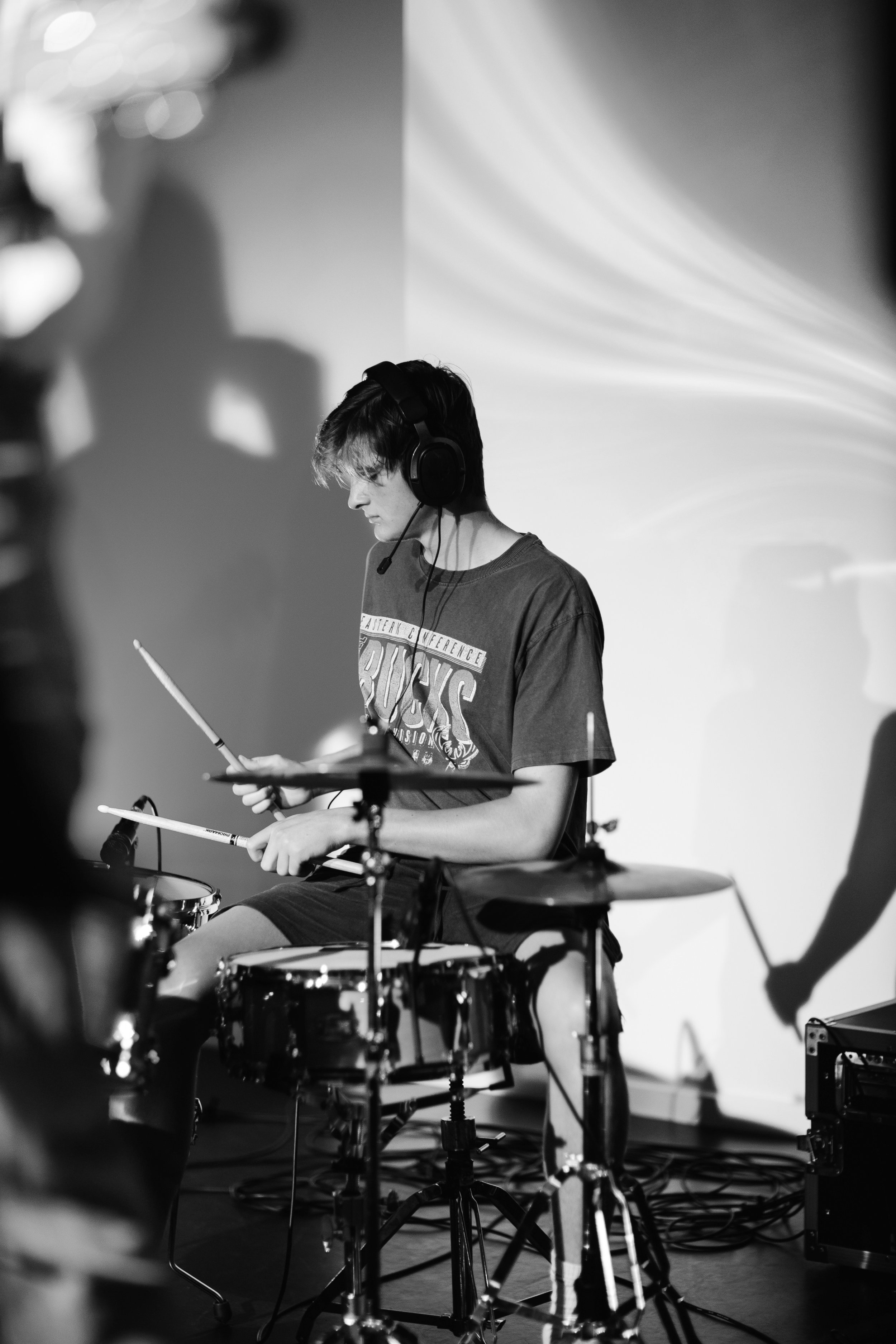 Luke, co-founder of vssls worship, playing drums wearing headphones and a t-shirt, in black and white.