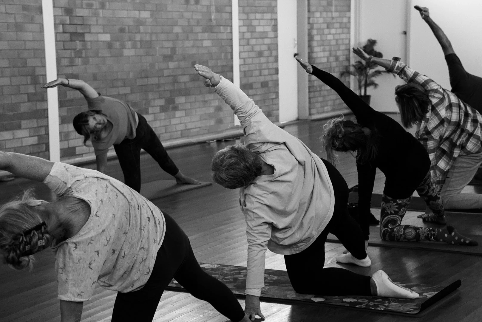 Group of people practicing yoga in a studio with brick wall, in various yoga poses.