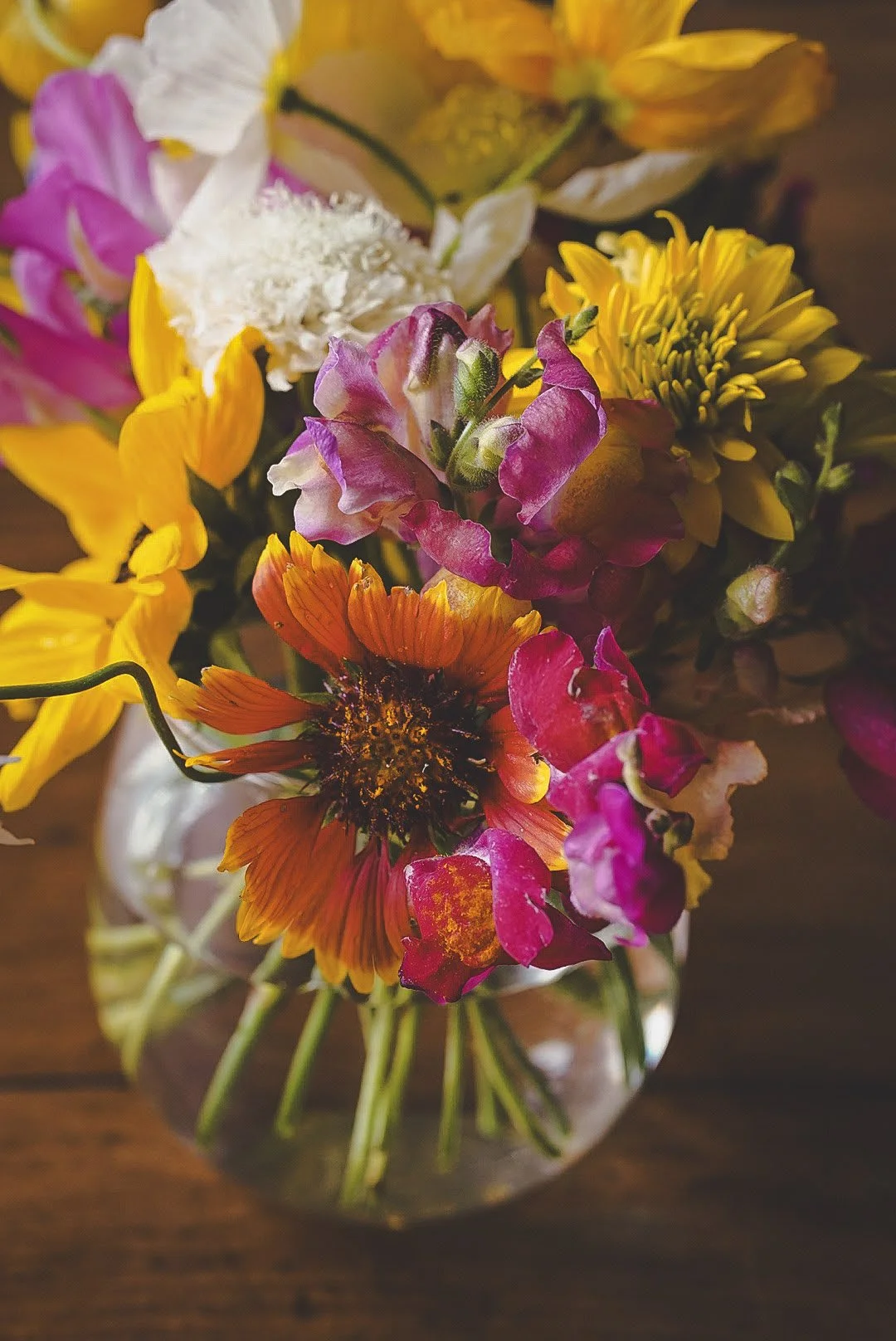 Colorful bouquet of various flowers in a glass vase on a wooden surface.