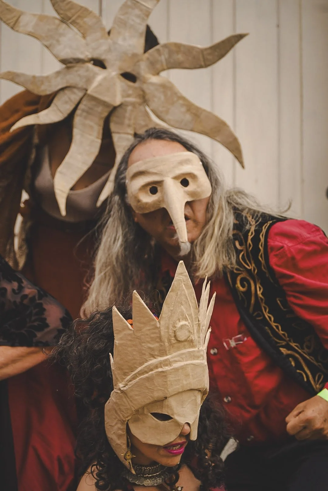 Two people wearing masks, one with a long nose mask and the other with a crown mask, and wearing costumes.