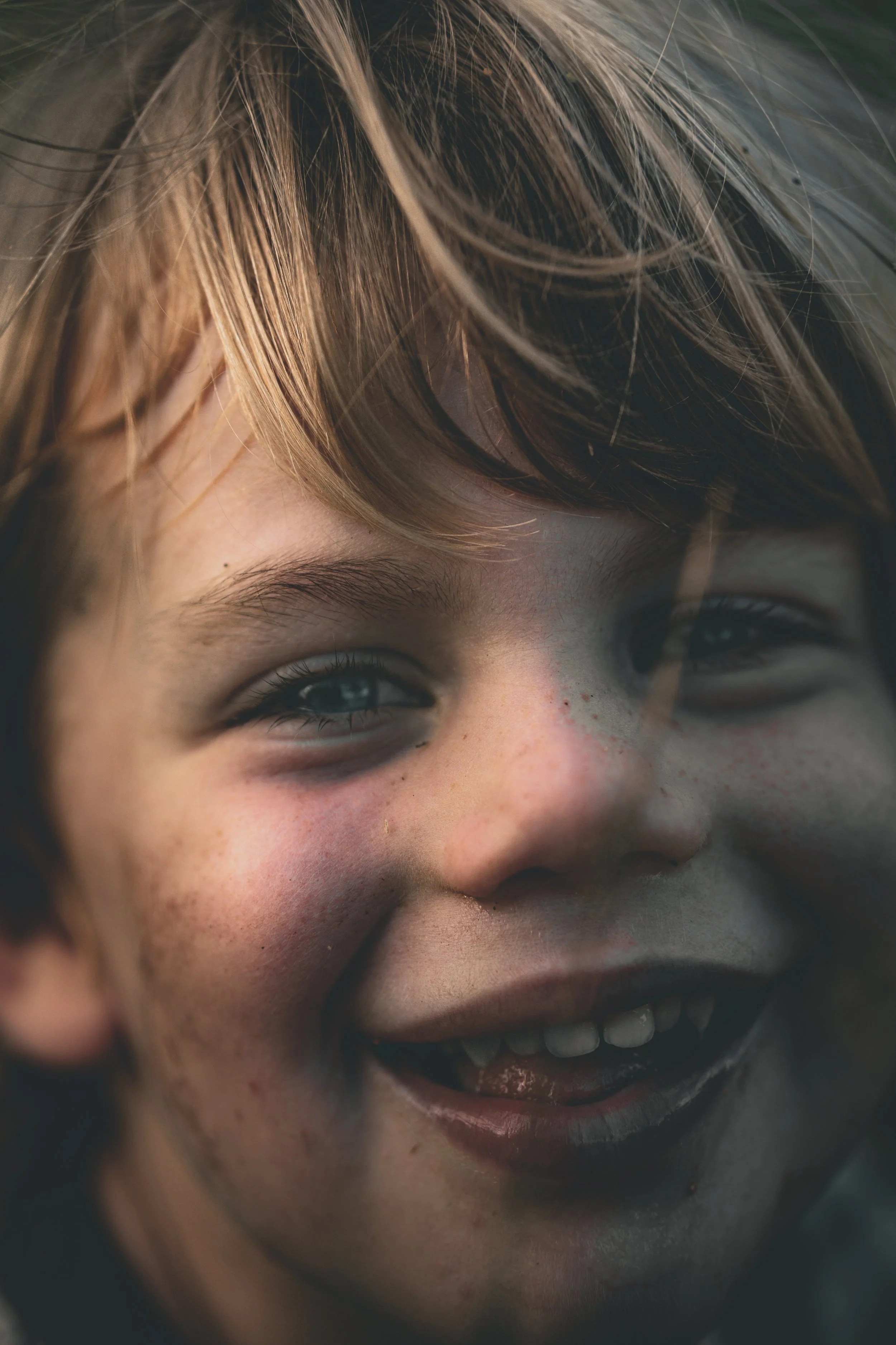 Close-up of a smiling young boy with blue eyes, freckles, and light brown hair.