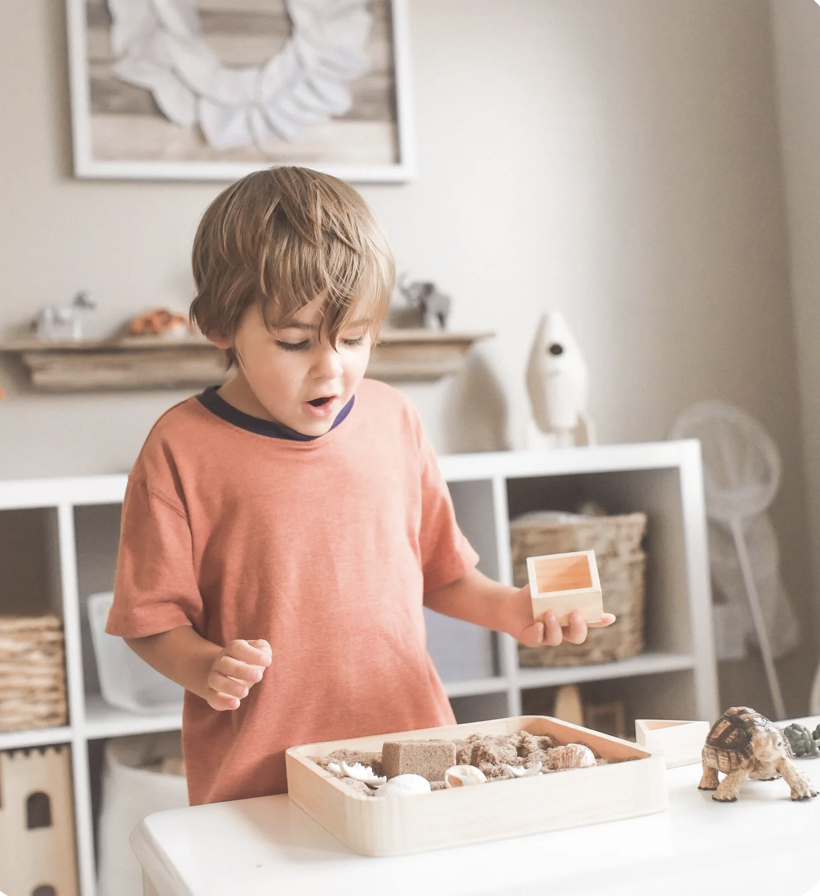 Little boy engaging in sensory play with sand excited