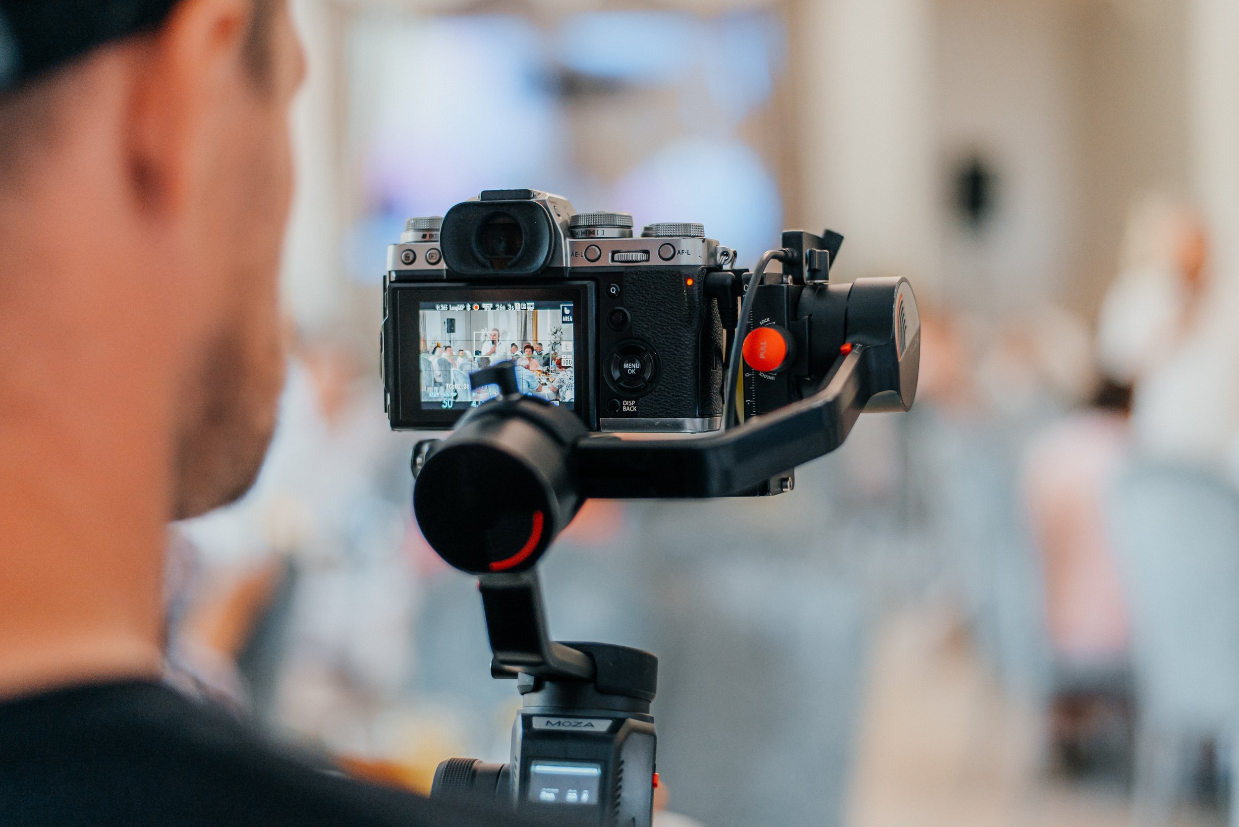 A person operating a camera on a tripod, capturing footage of a crowded indoor event.
