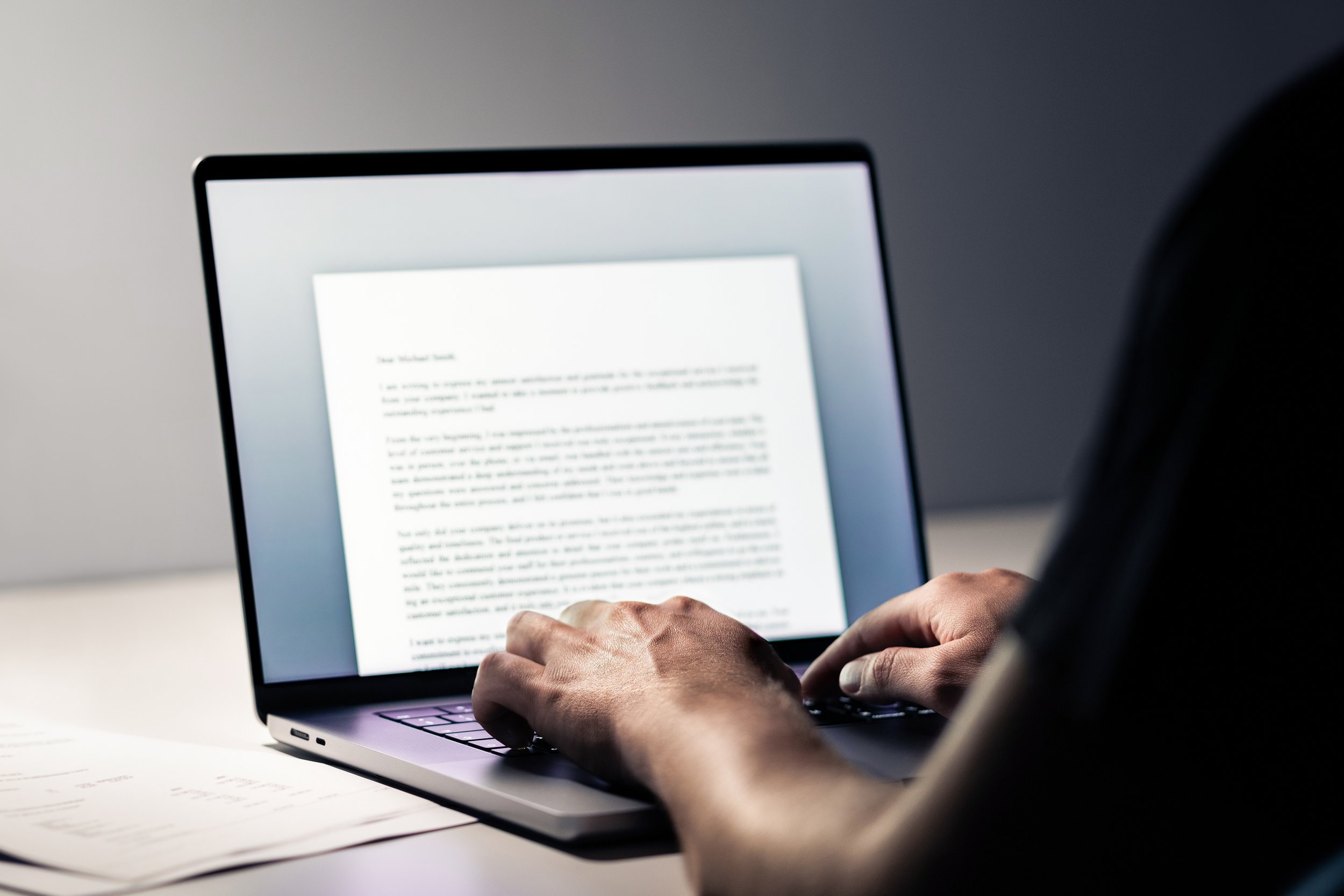 Person typing on a laptop with a blurry document on the screen.