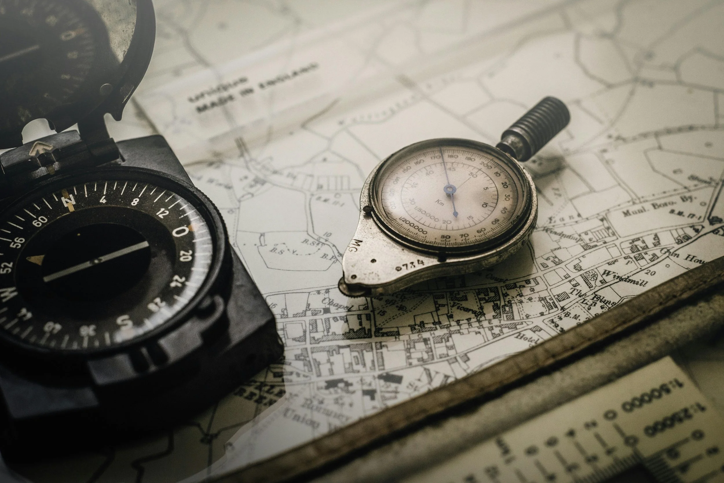 A compass, a stopwatch, and a map spread out on a surface, suggesting navigation or planning.