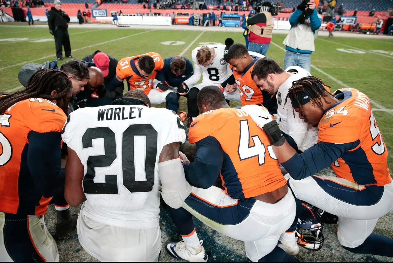 American football players from the Denver Broncos and the Los Angeles Rams praying together on the field during a game.