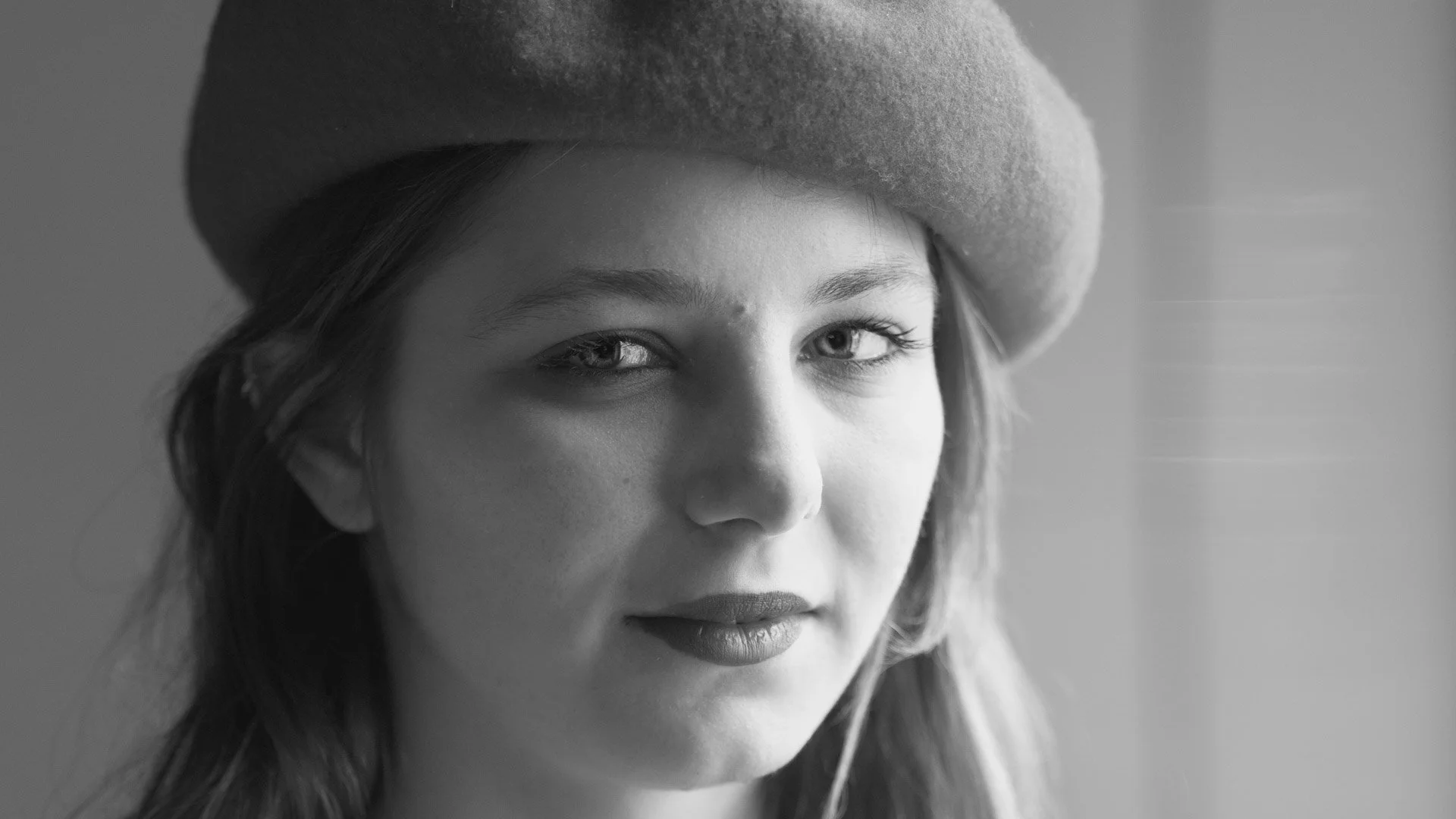Close-up black and white portrait of a young woman wearing a hat, looking thoughtfully towards the camera.