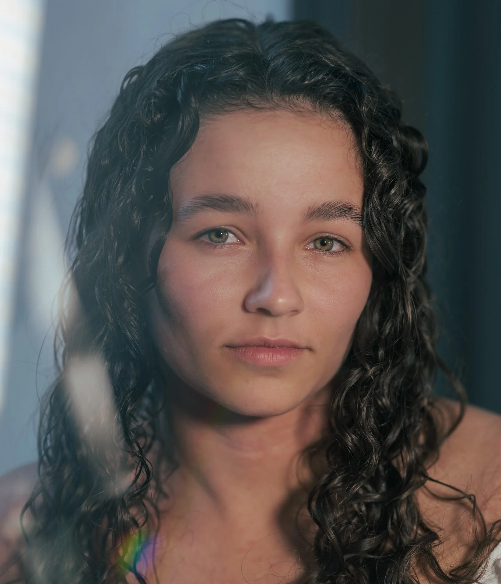 Close-up of a woman with curly hair and piercing blue-green eyes looking at the camera