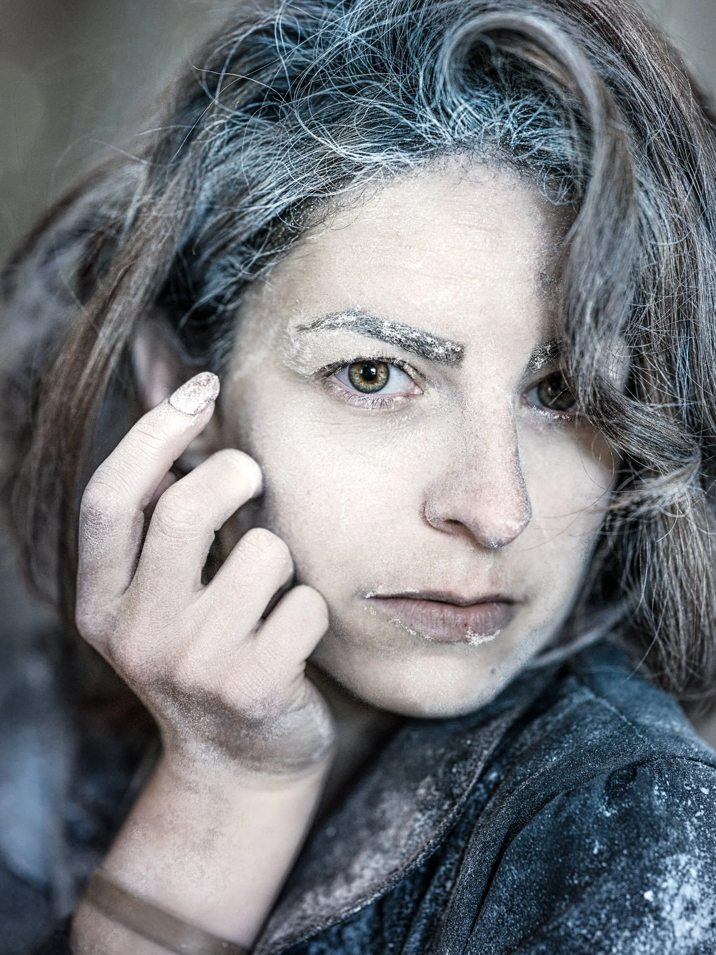 Close-up of a woman with dust or flour on her face and hand, with messy hair and intense gaze.