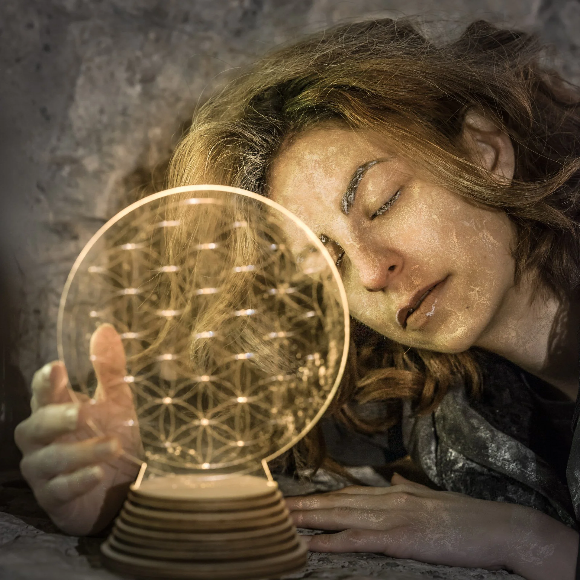A person sleeps with their face resting on the ground, eyes closed, in front of a geometric light sculpture.