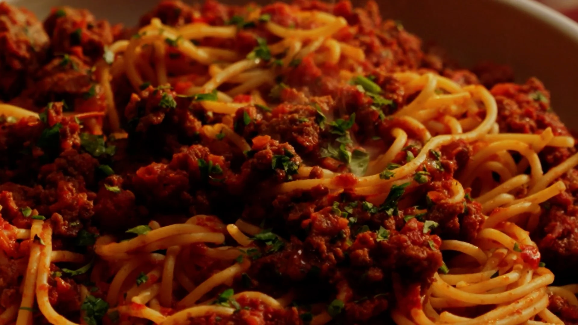 Close-up of cooked spaghetti topped with meat sauce and garnished with chopped parsley.