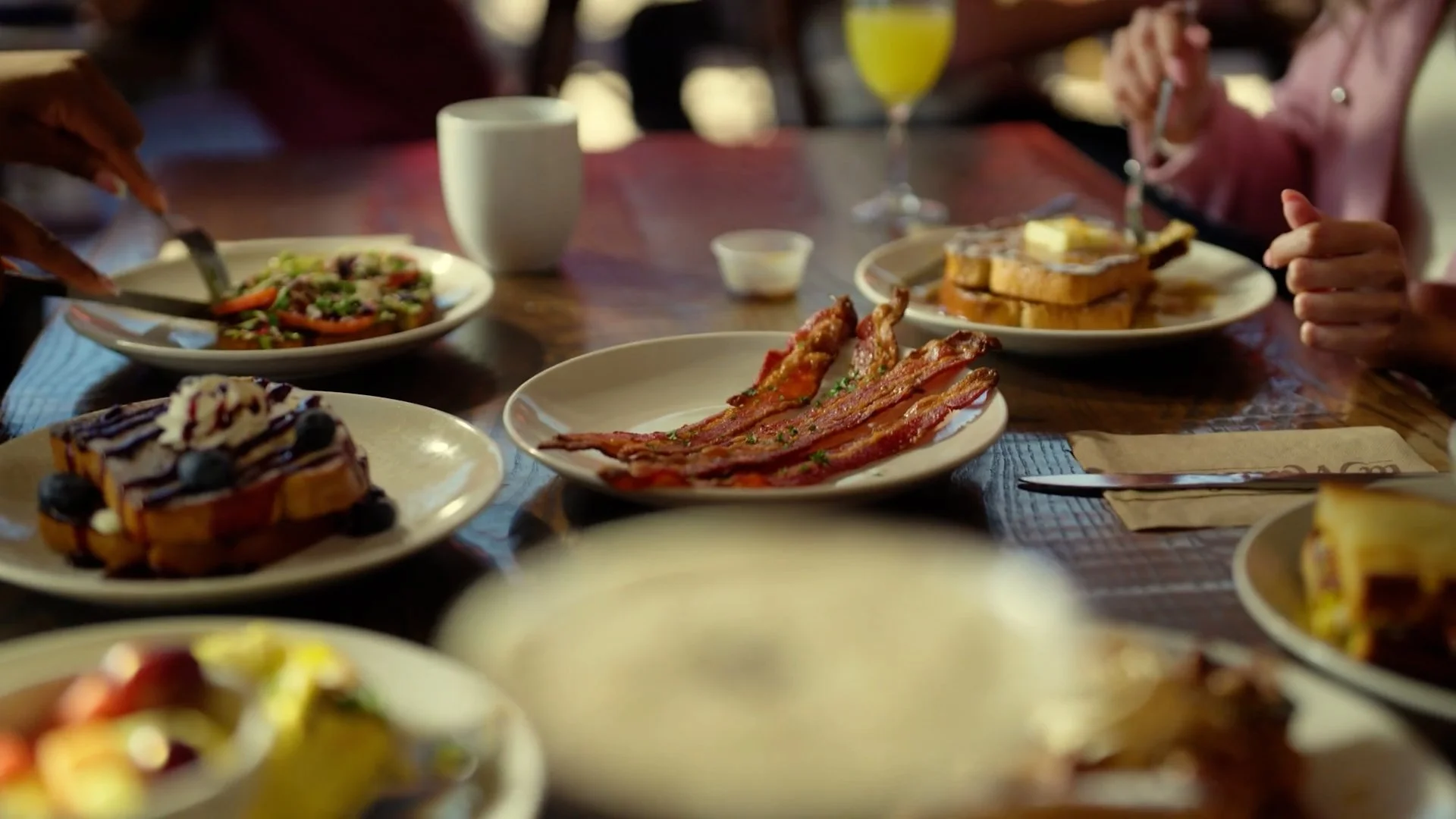A table with breakfast foods including bacon, French toast with blueberries, a salad, and a glass of orange juice.