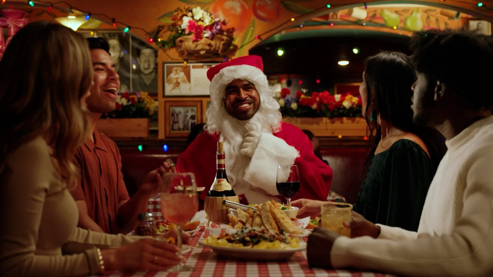 A group of people celebrating Christmas at a restaurant with a man dressed as Santa Claus, surrounded by festive decorations, food, and drinks.