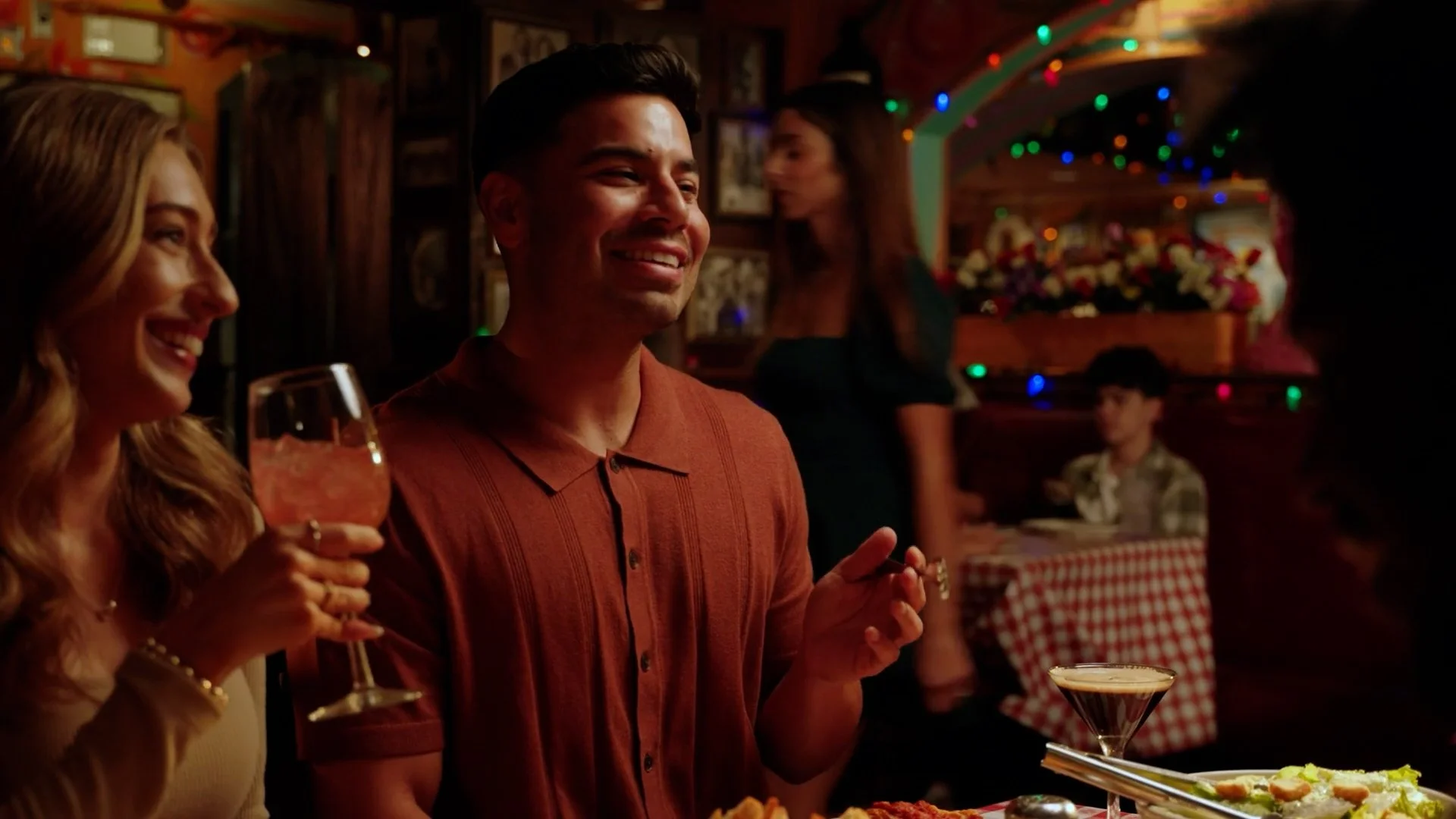 People enjoying a meal at a festive restaurant with colorful lights and decorations, including a woman holding a glass of wine and a smiling man sitting beside her.