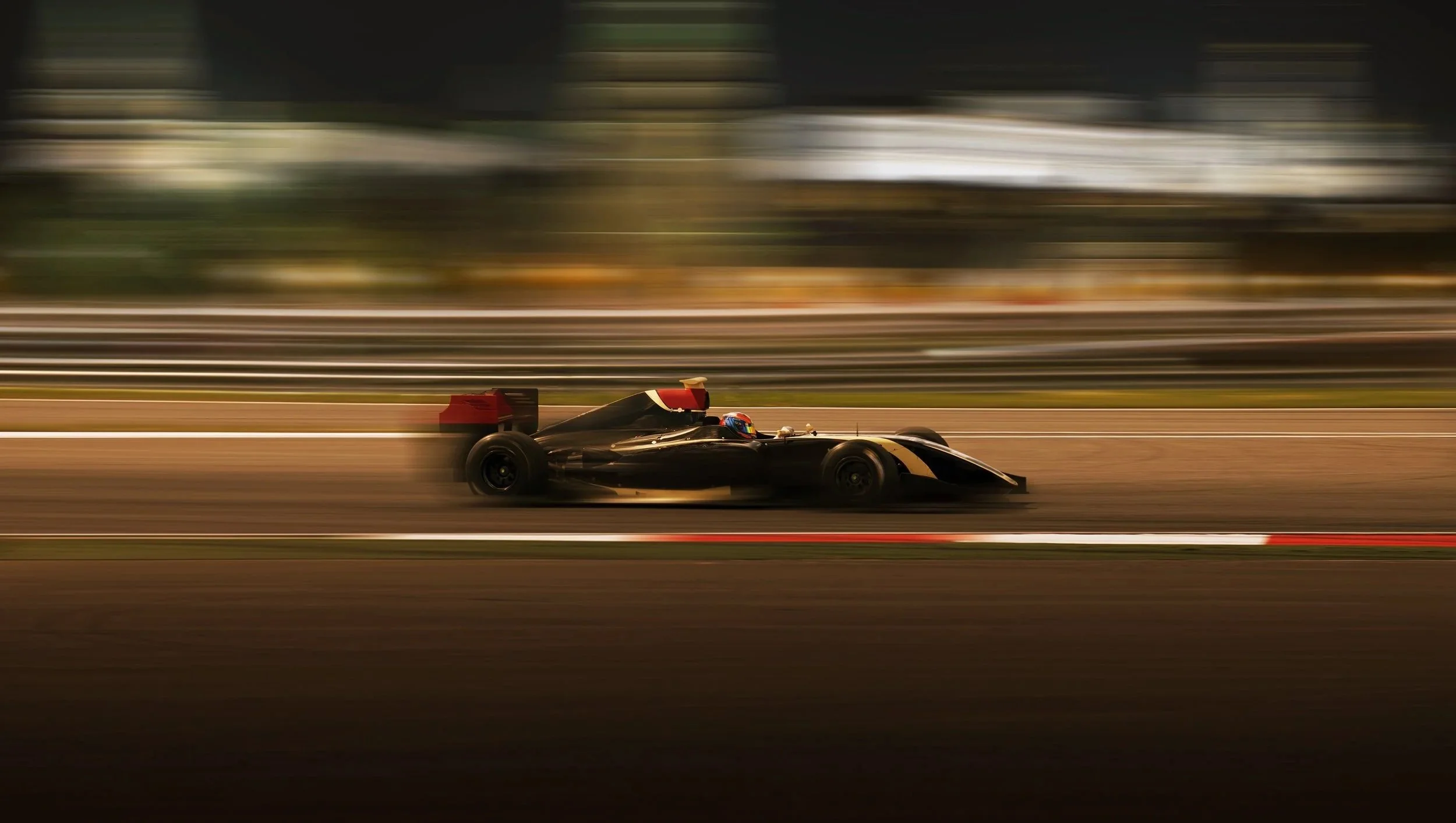 A black Formula 1 race car speeding on a racetrack at night with motion blur.