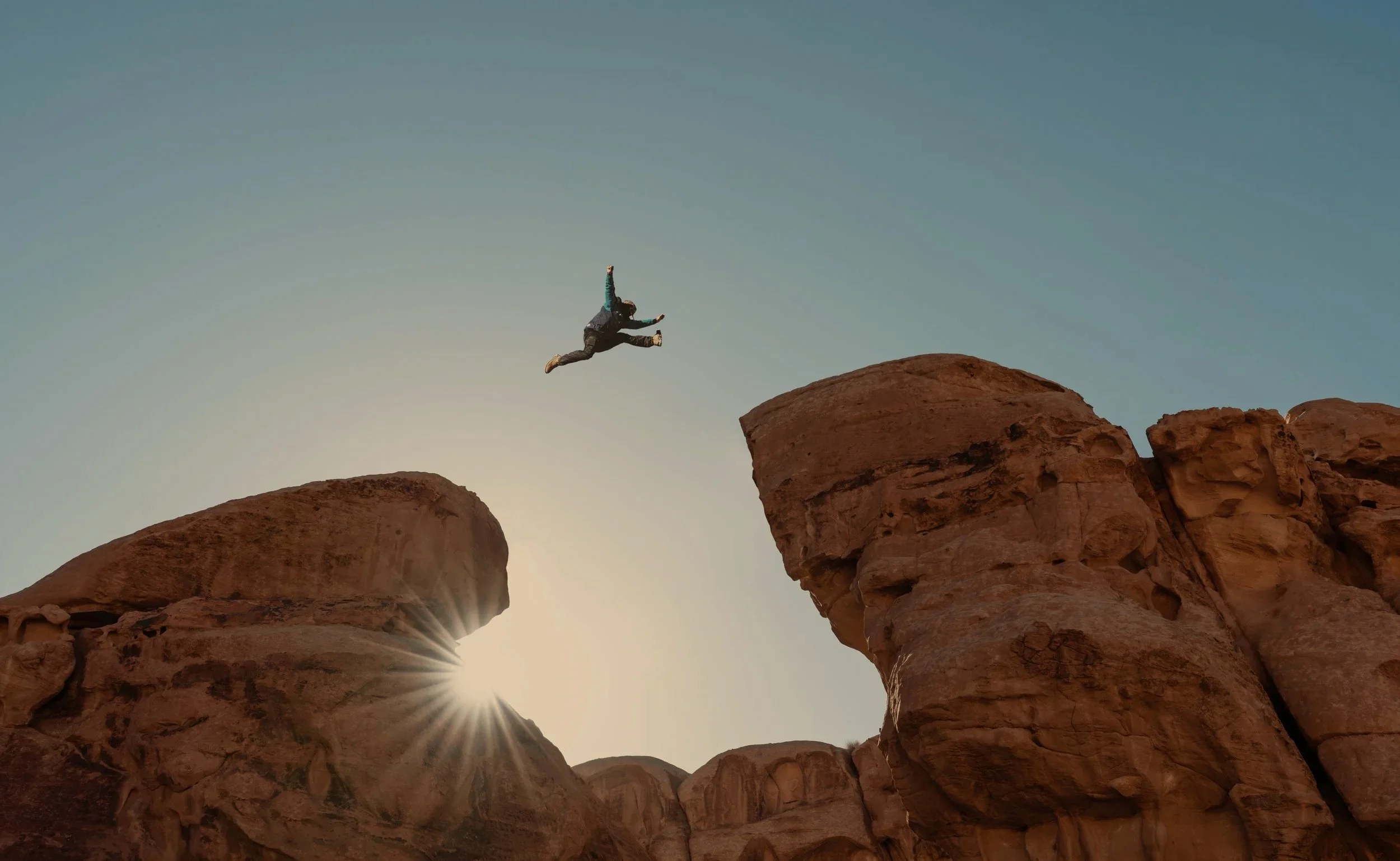 A person jumping between two large rock formations at sunset or sunrise.