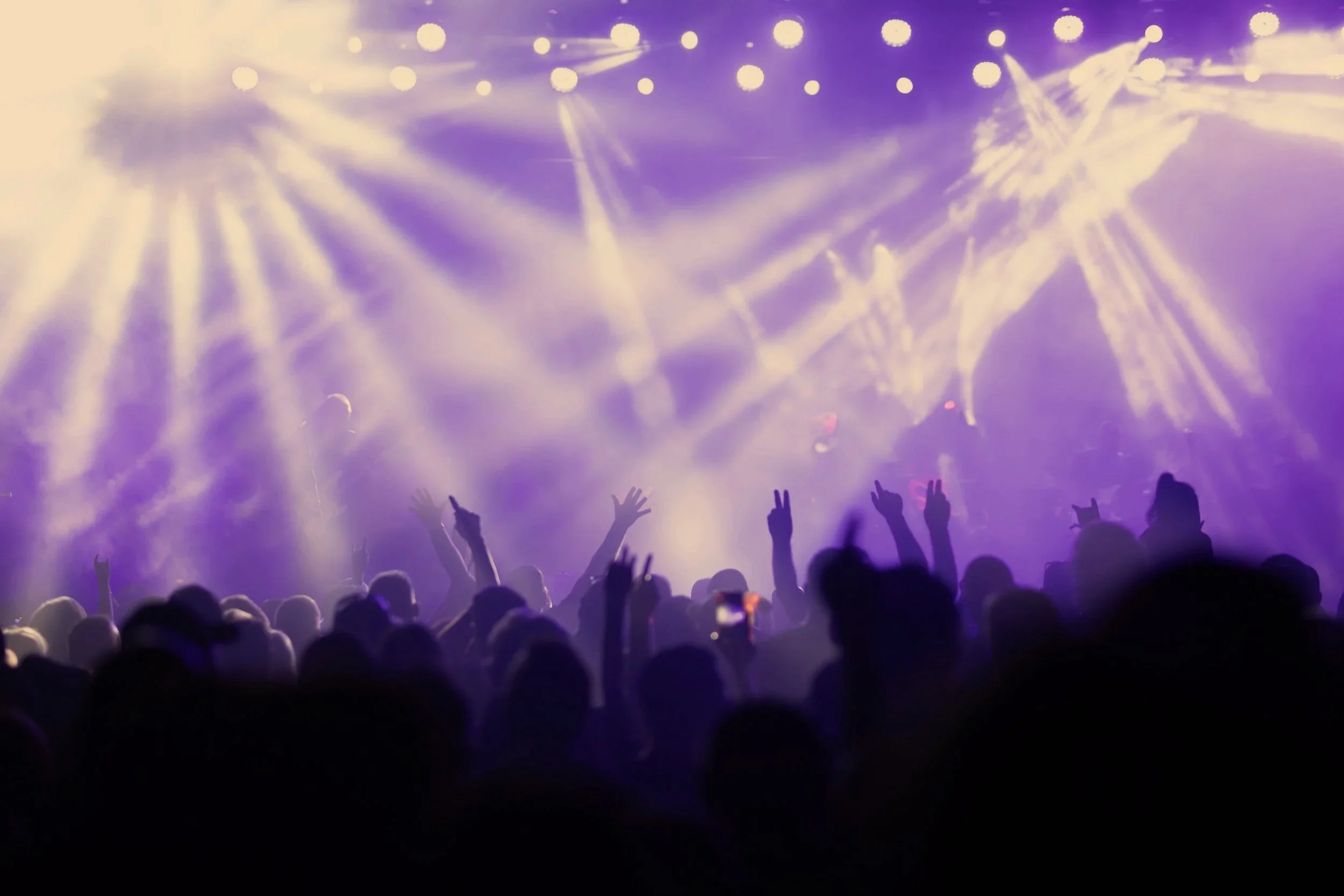 Crowd at a concert with colorful stage lights and laser beams.