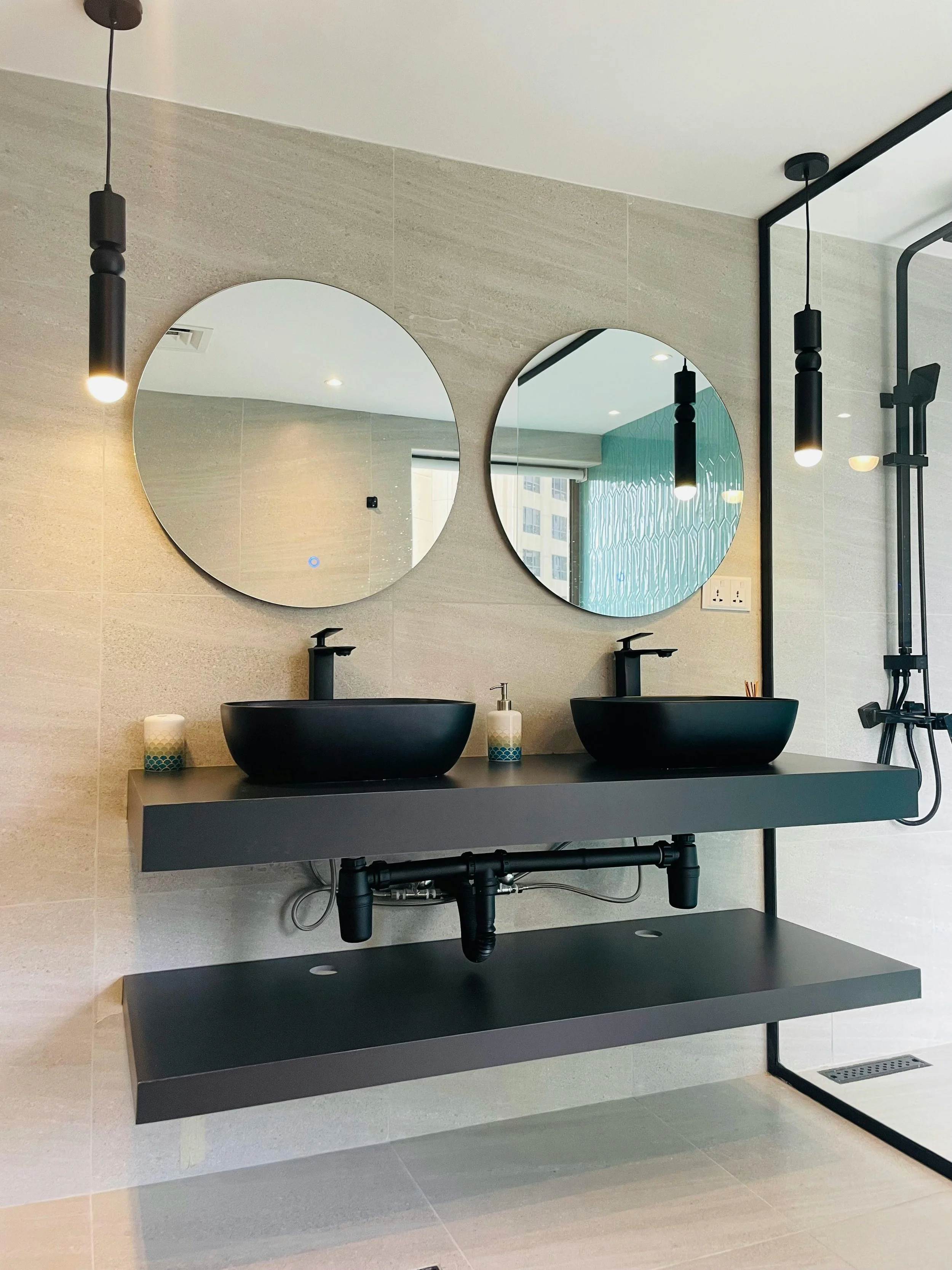 RC Squared Modern bathroom remodel vanity with two black vessel sinks, round mirrors, and black pendant lights, with a shower area on the right.