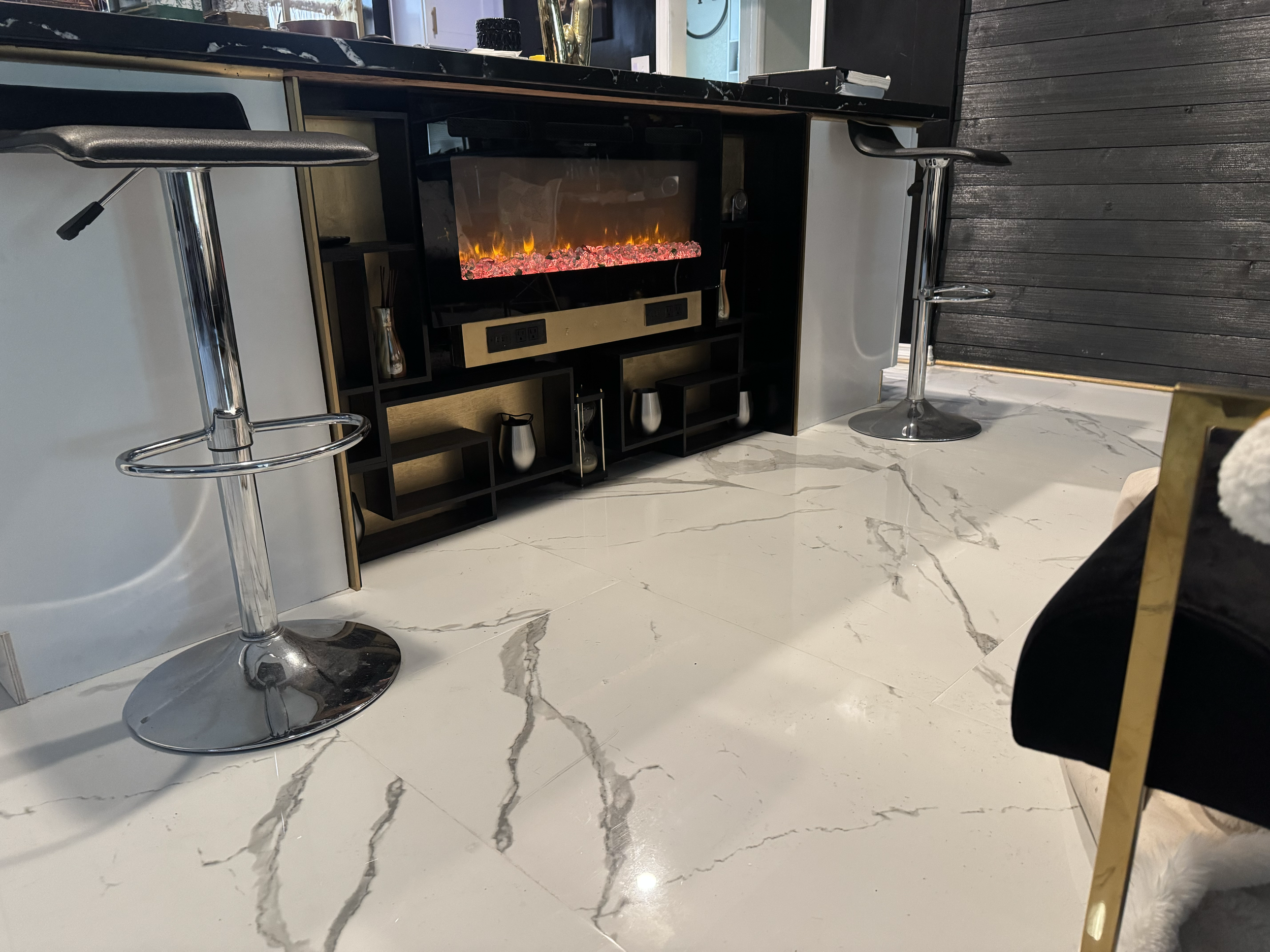 Modern reception area with white marble floor, black bar-height chairs, and a black entertainment unit with an electric fireplace.