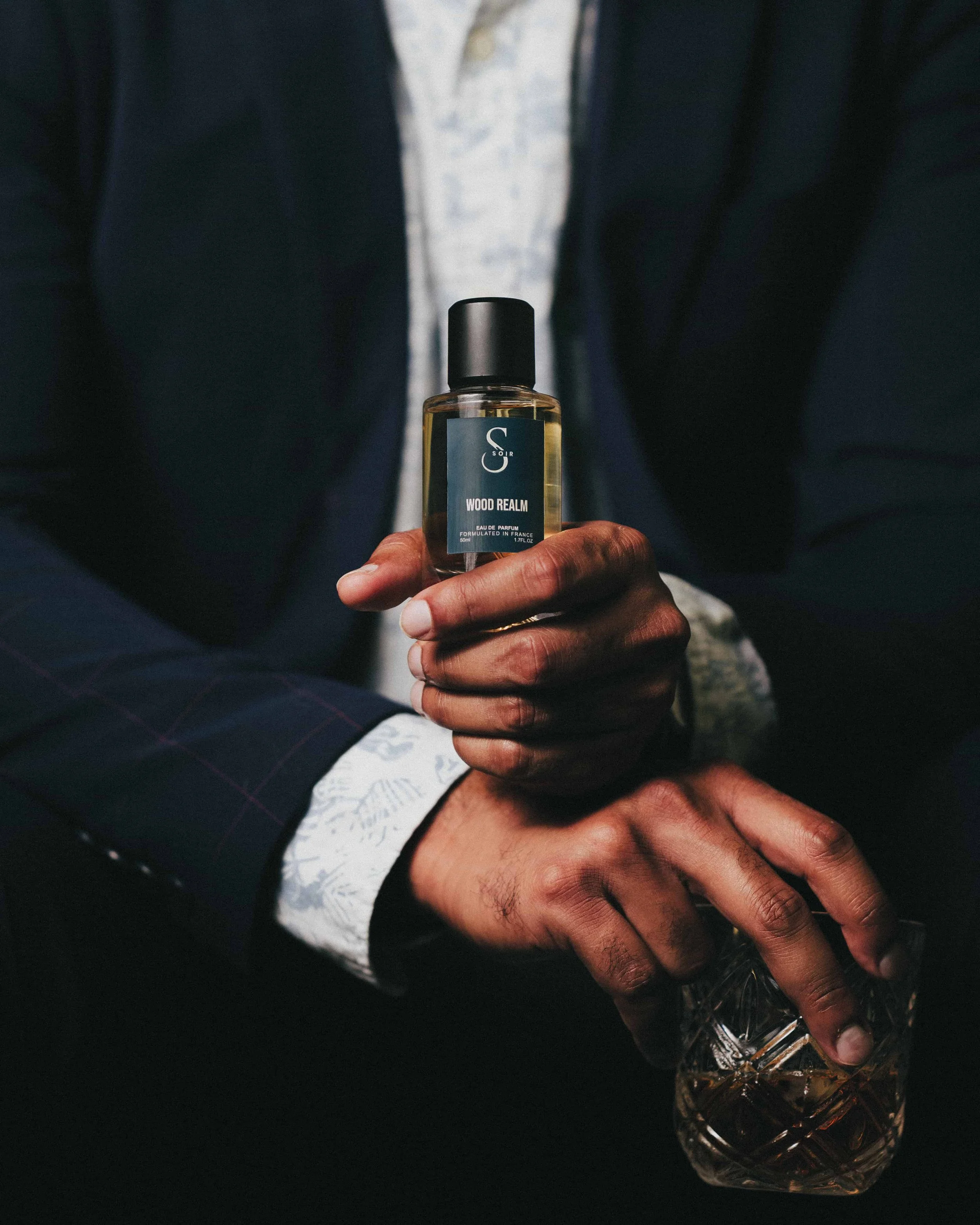 man holding a glass of wihsky and a bottle of perfum