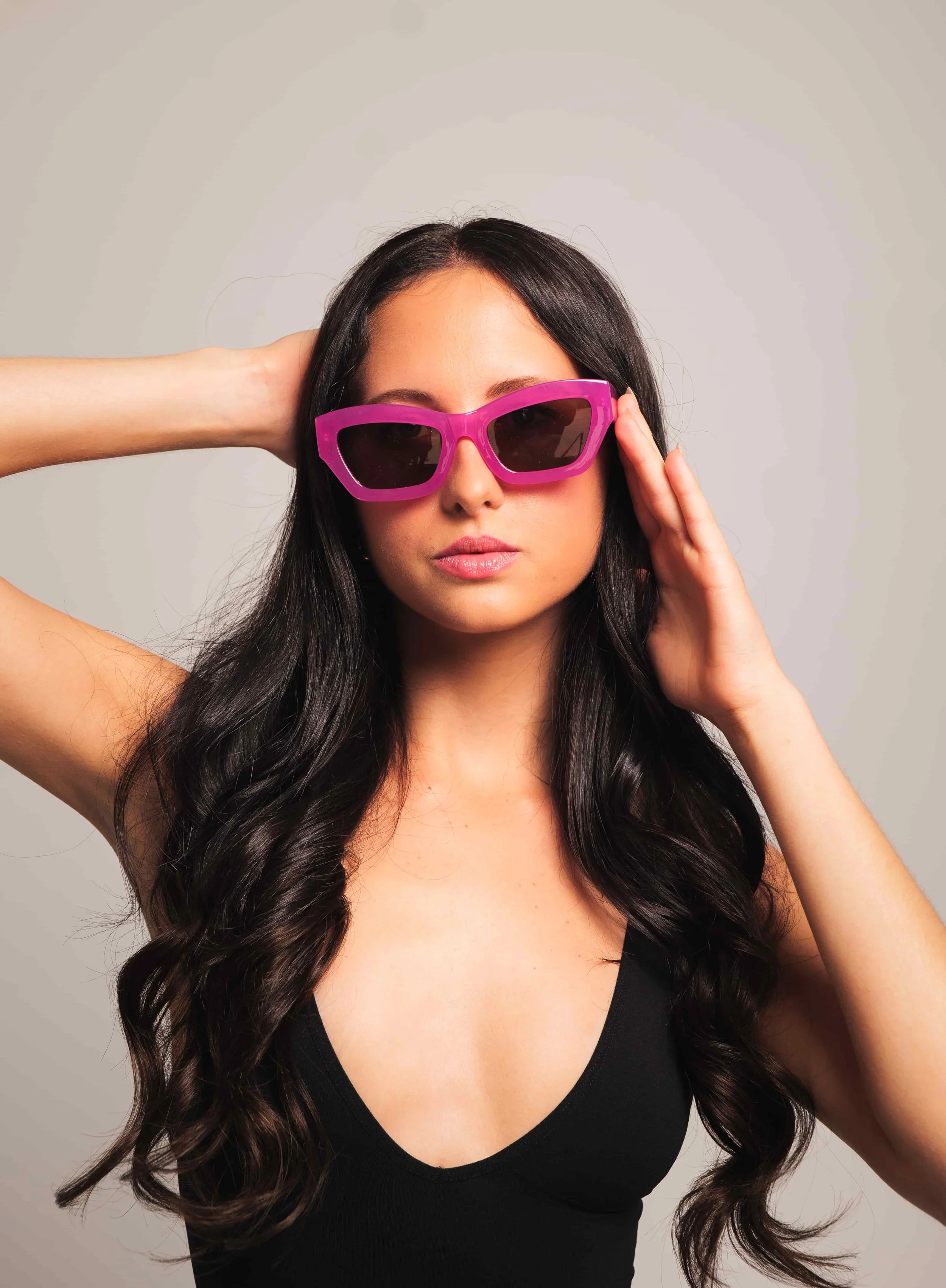 woman with purple sunglasses and wavy hair posing on a neutral studio background. Professional lifestyle photography for modern entrepreneurs.