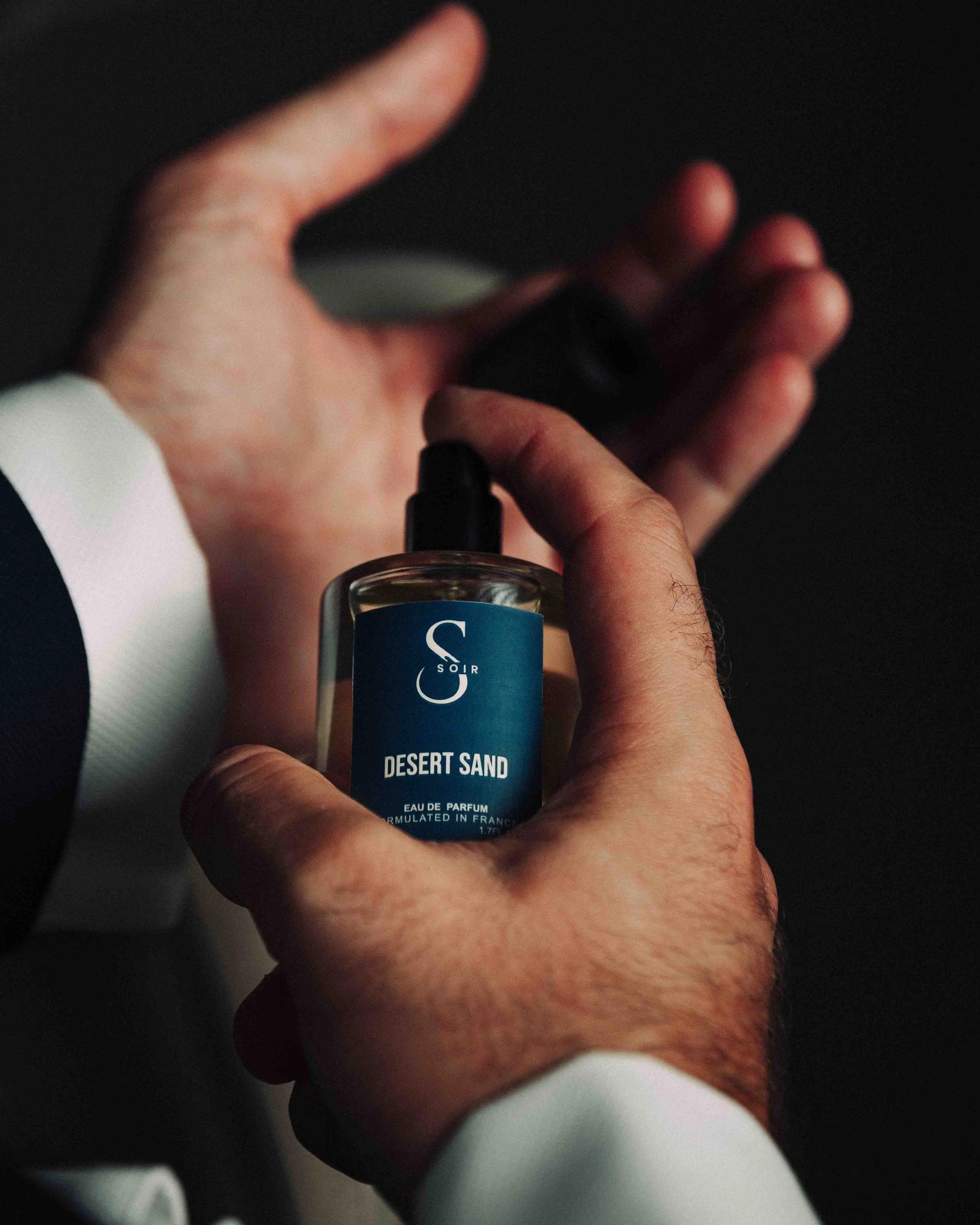 man's wearing a suit spraying some perfum on his wrist